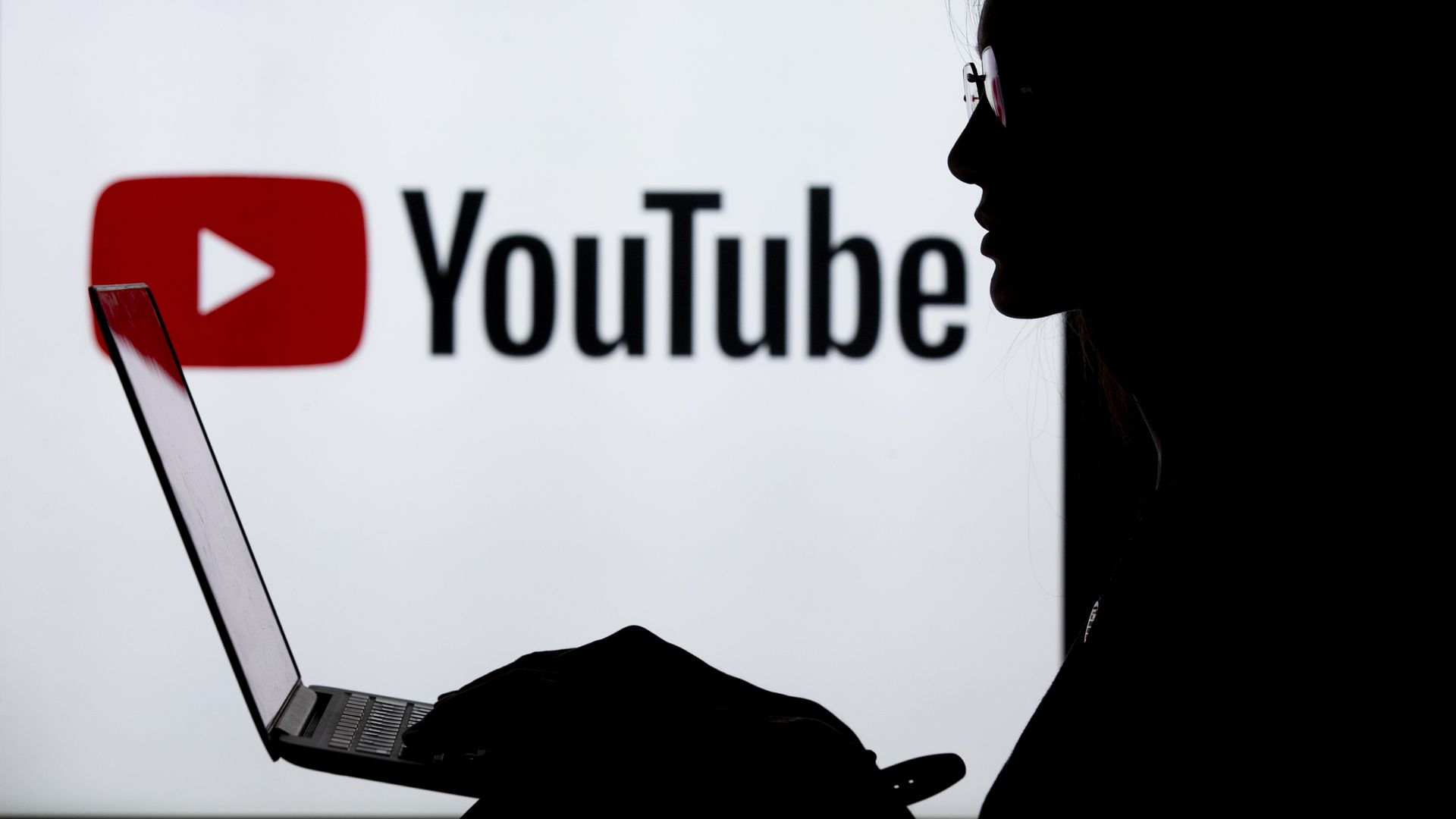 A silhouette of a woman with a laptop in front of the YouTube logo
