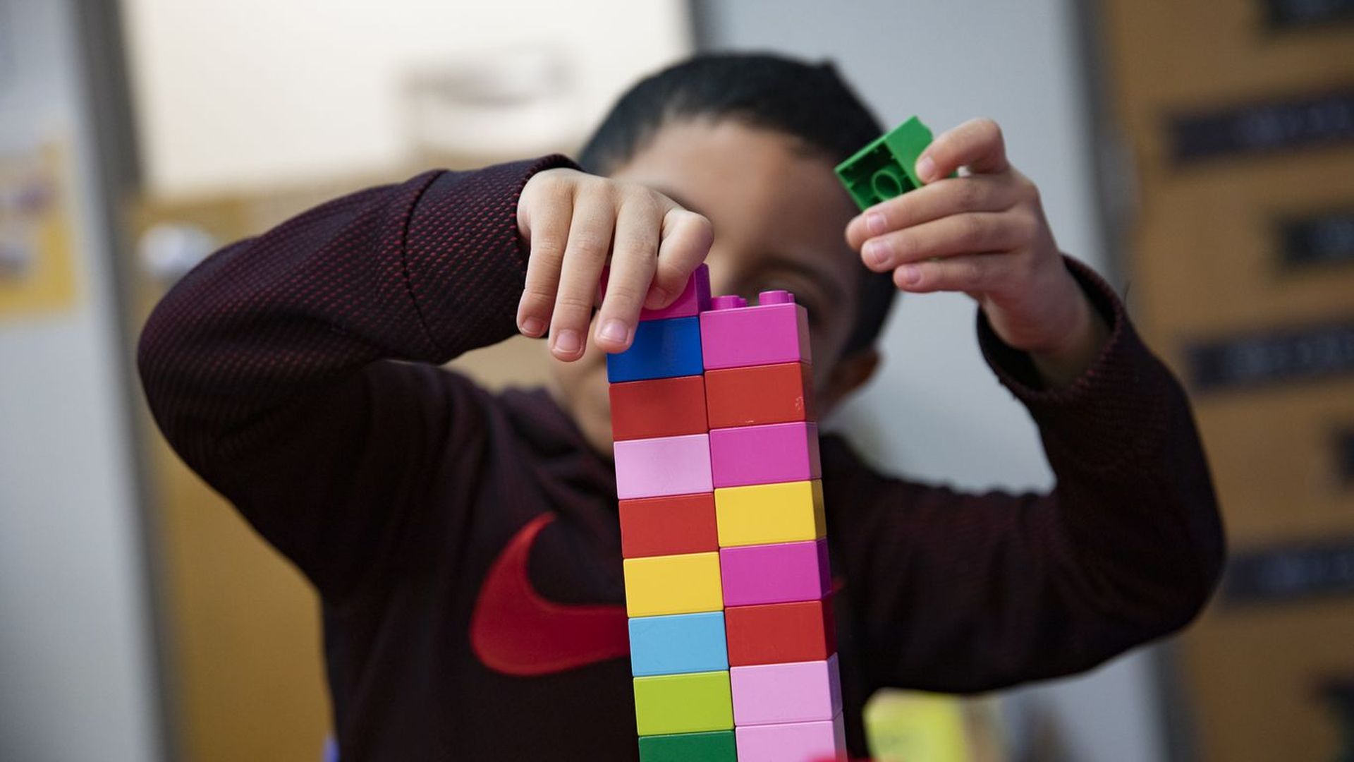 A child stacks multicolored Duplo building blocks