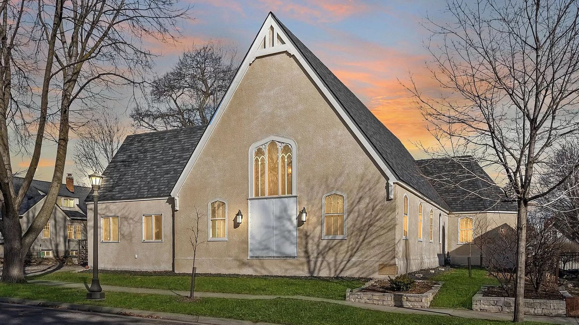 The exterior of a church with yellow stucco and large windows.