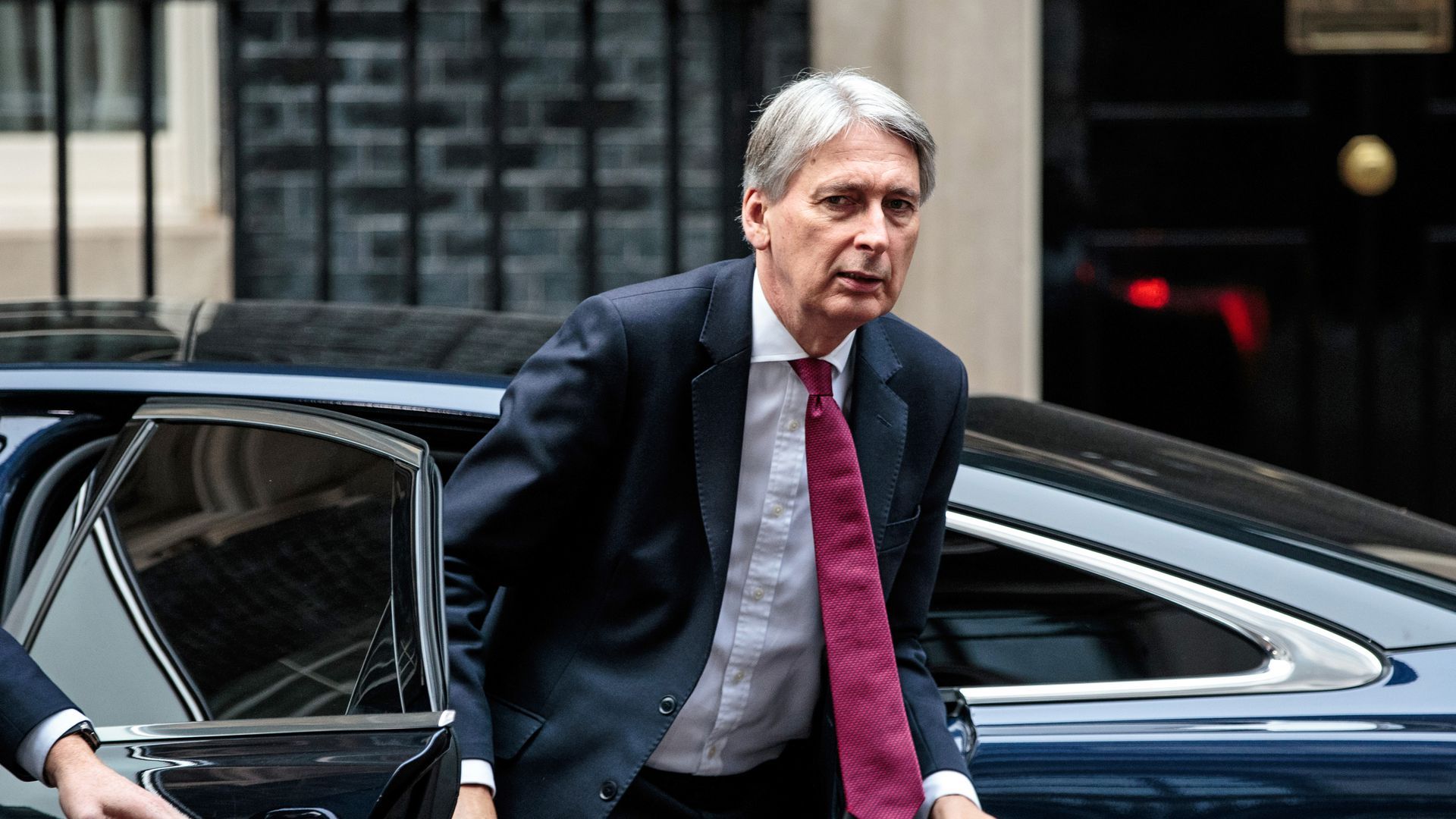U.K. Chancellor Philip Hammond steps out of a car while glancing at the camera