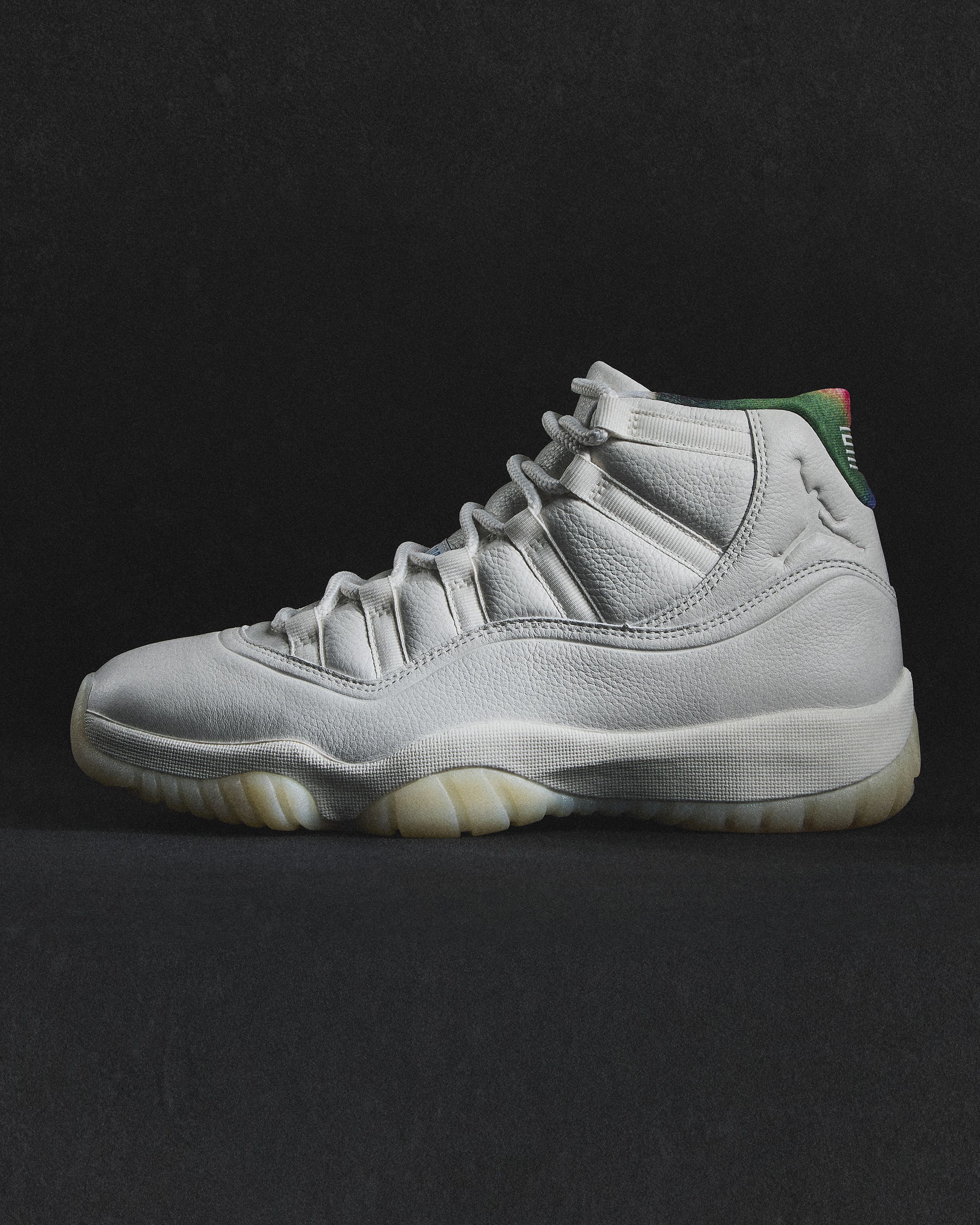 White high-top sneaker with textured leather, translucent sole, and multicolored green to red gradient on the heel collar against a black background.