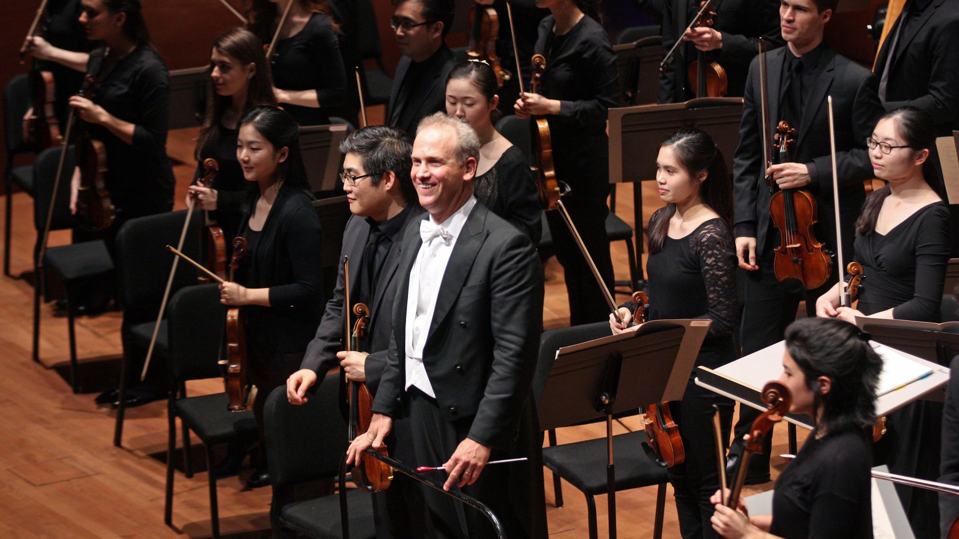 A conductor stands in front of an orchestra. 