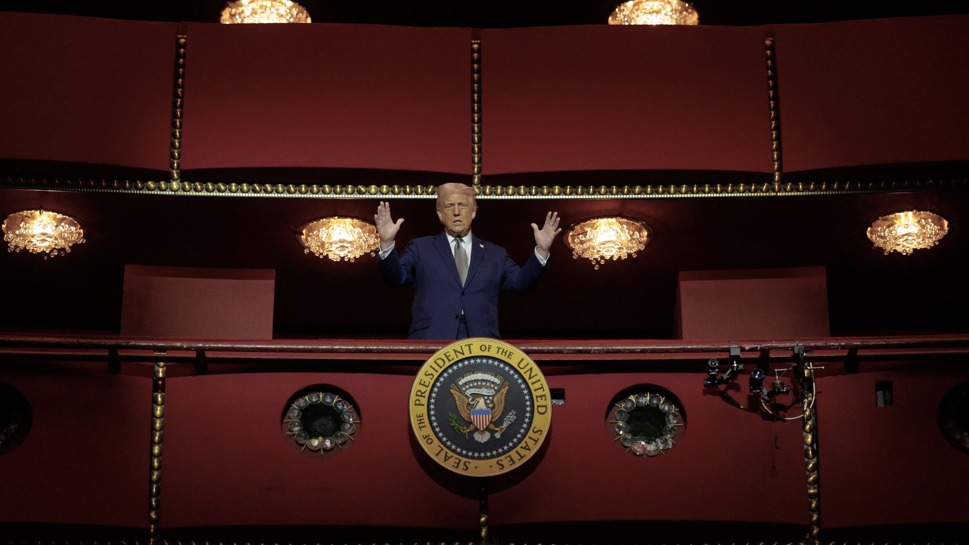 President Trump stands with his hands up in the air from a booth in the Kennedy Center.