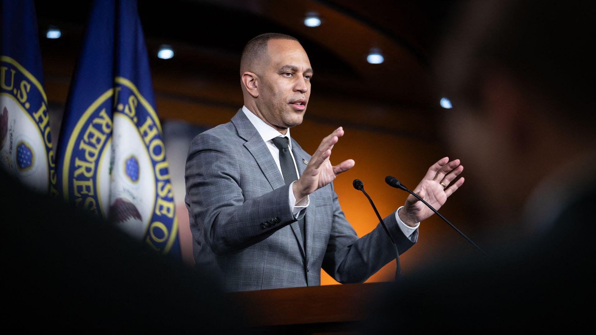 House Minority Leader Hakeem Jeffries, wearing a gray suit and speaking at a podium.