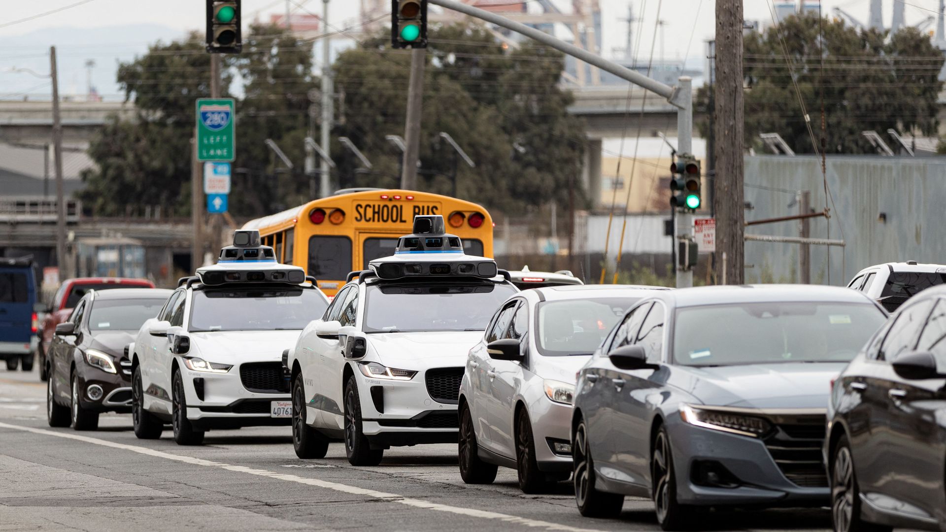 Photo of traffic in San Francisco, including two Waymo self-driving cars, and a school bus going in the opposition direction. 