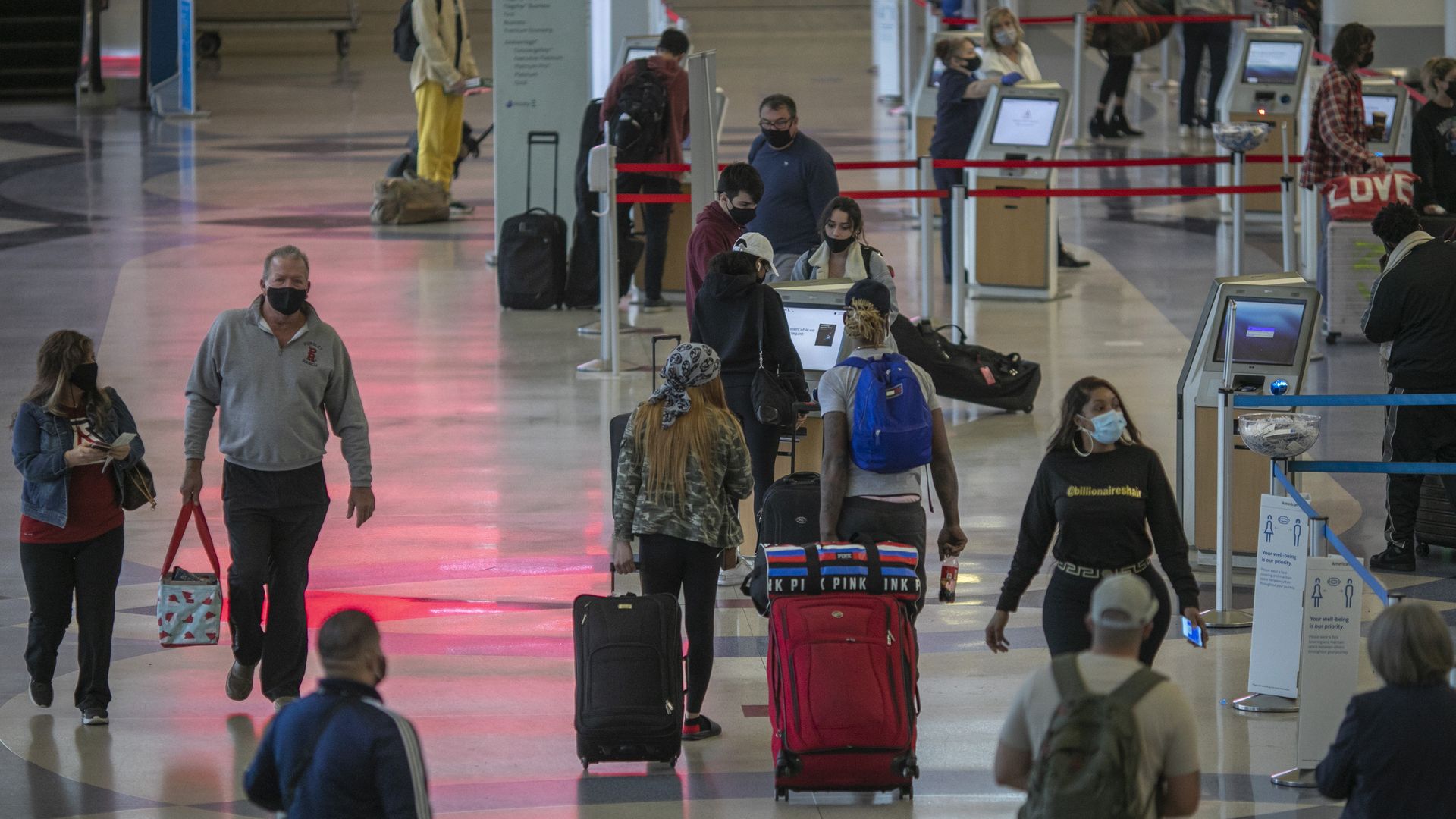 A crowd of people walking in different directions in an airport, most carrying luggage and all wearing masks