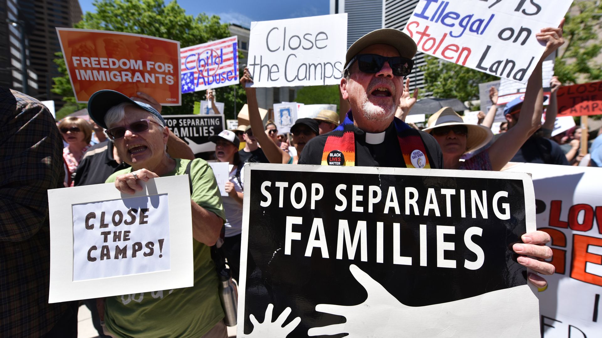 Protestors holding signs opposing Trump immigration policies. One says "Stop separating families"