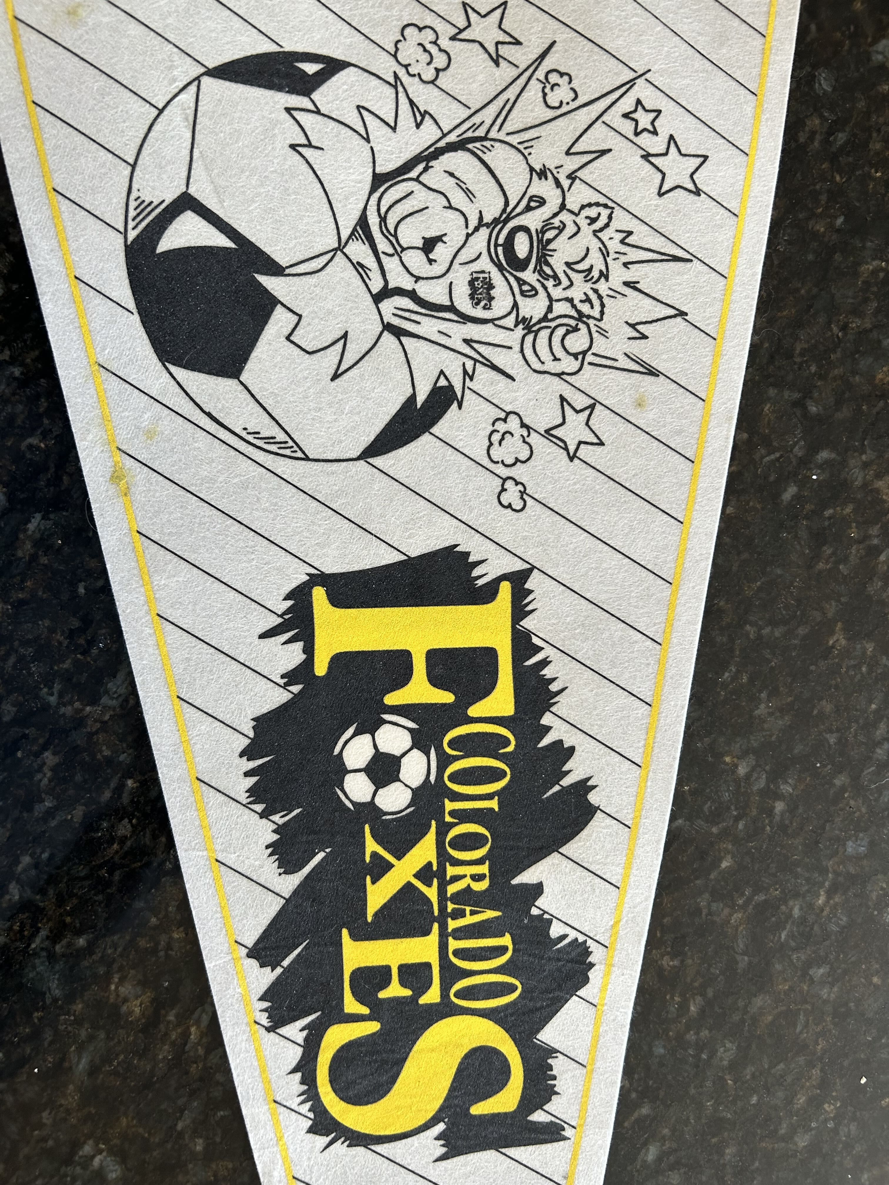 Comic-style black-and-white drawing of a soccer player kicking a ball with motion lines and stars; a yellow-bordered banner with bold yellow text sits below.