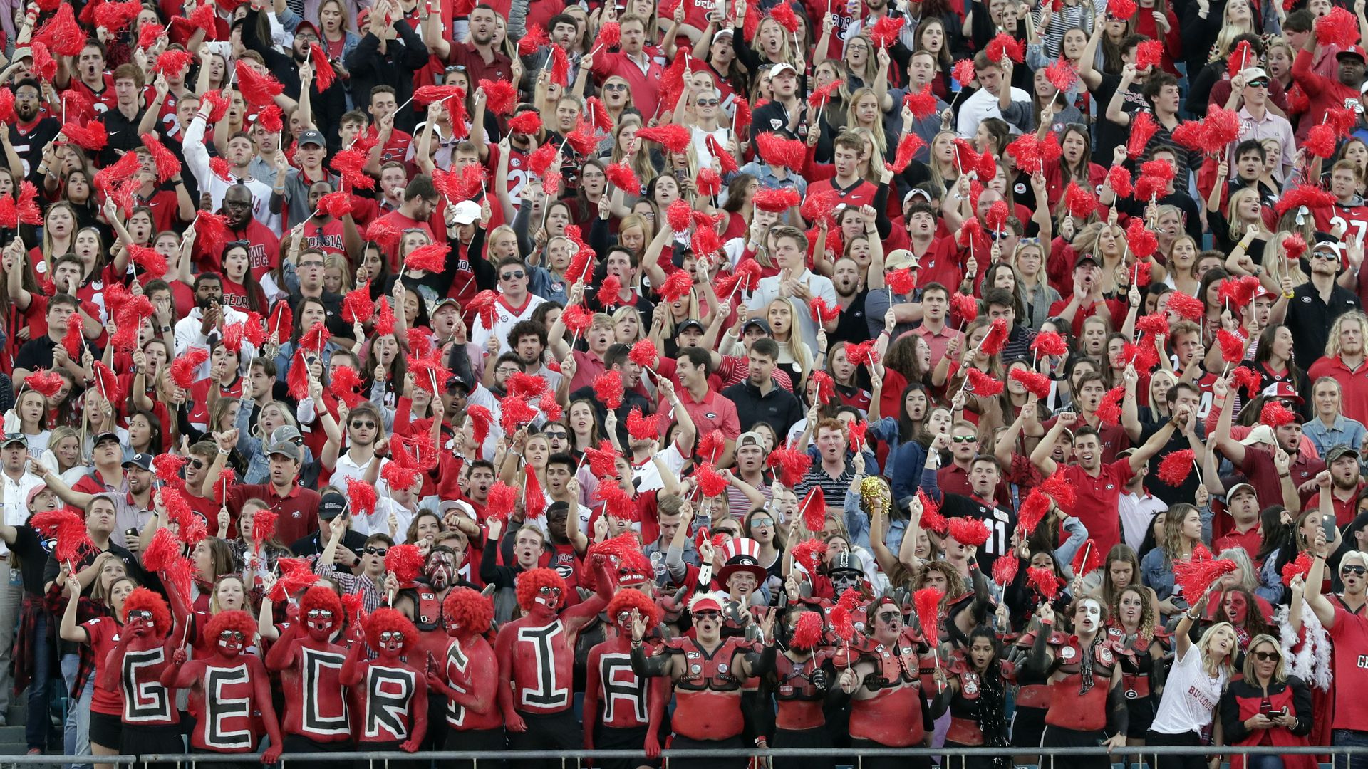 Fans wearing red, black, and white stand in the UGA fan section and cheer