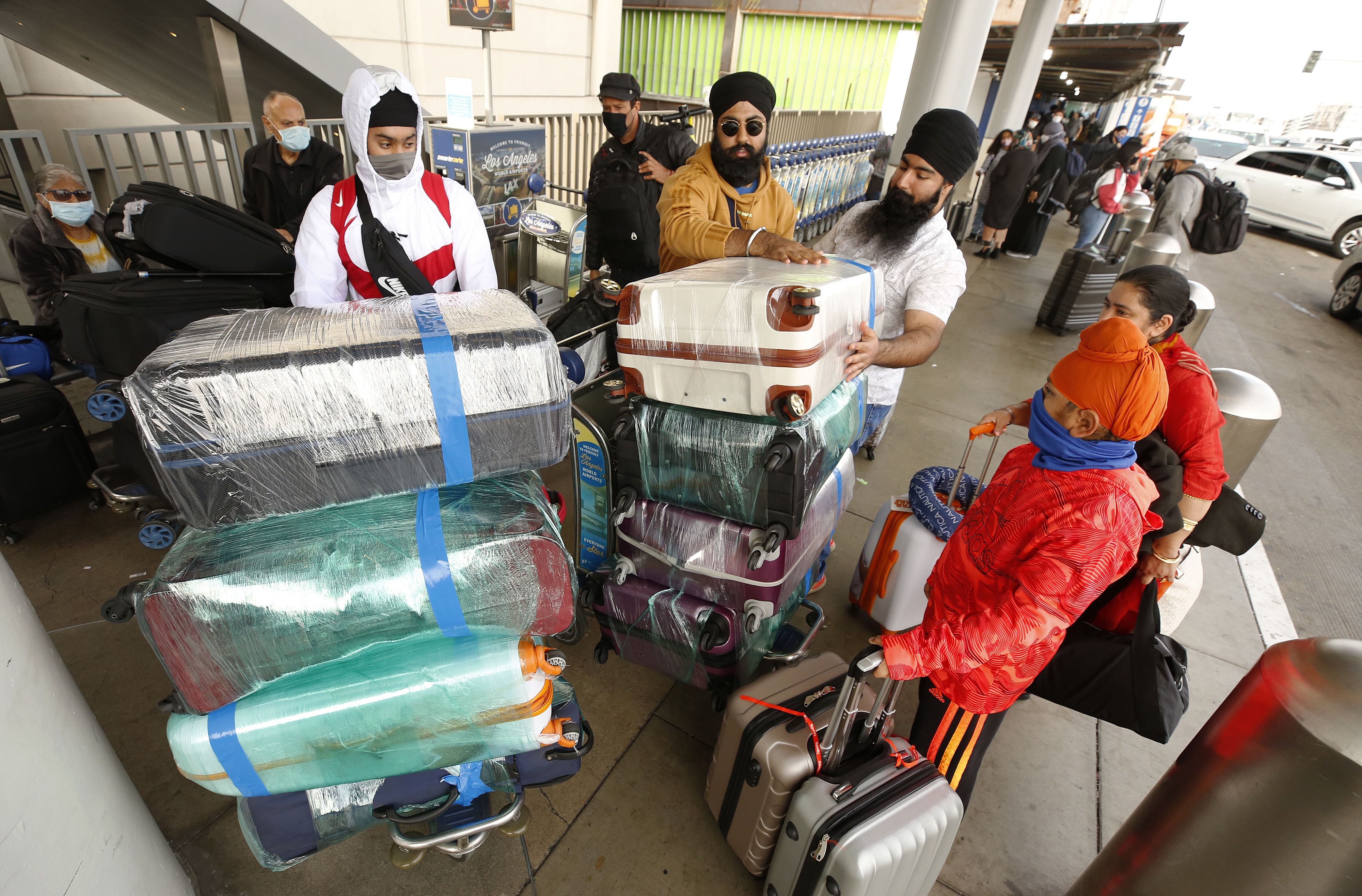 Photo of people with two carts filled with luggage as they stand outside an airport terminal