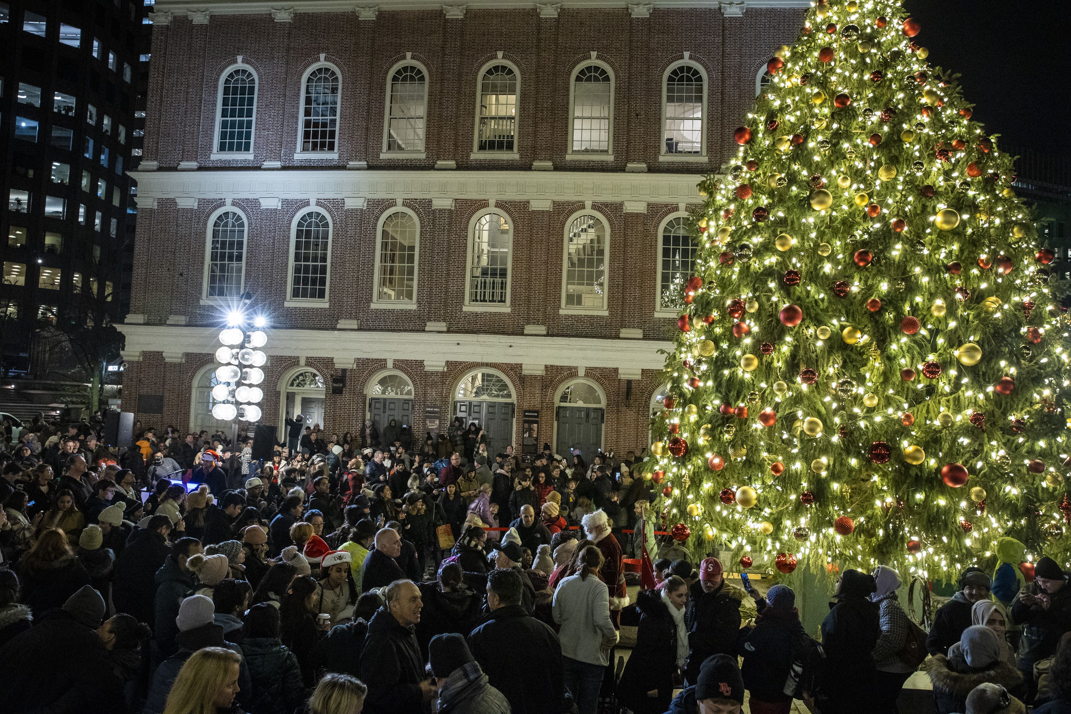 A brick building in Faneuil Hall with a lit up Christmas tree and a big crowd in front of it. 