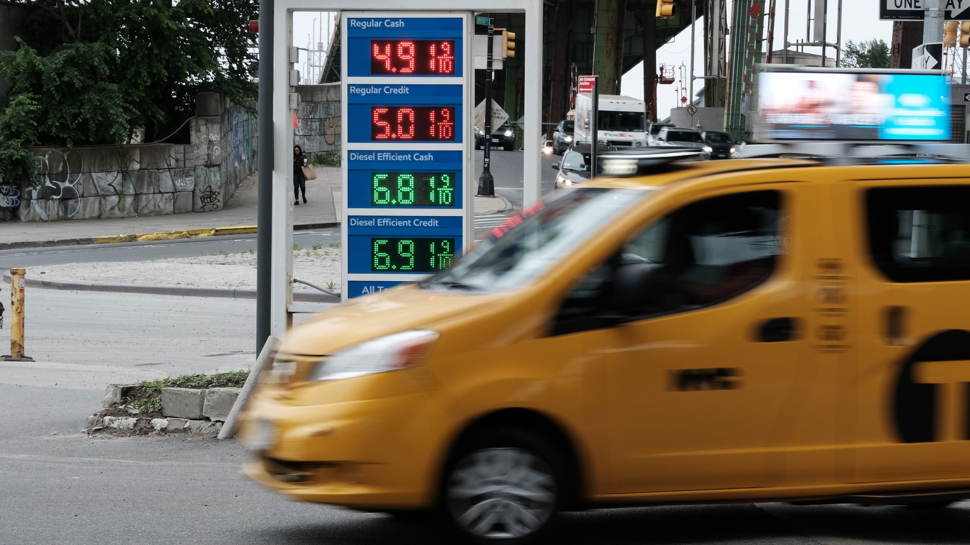 Yellow taxi cab driving in front of a gas station