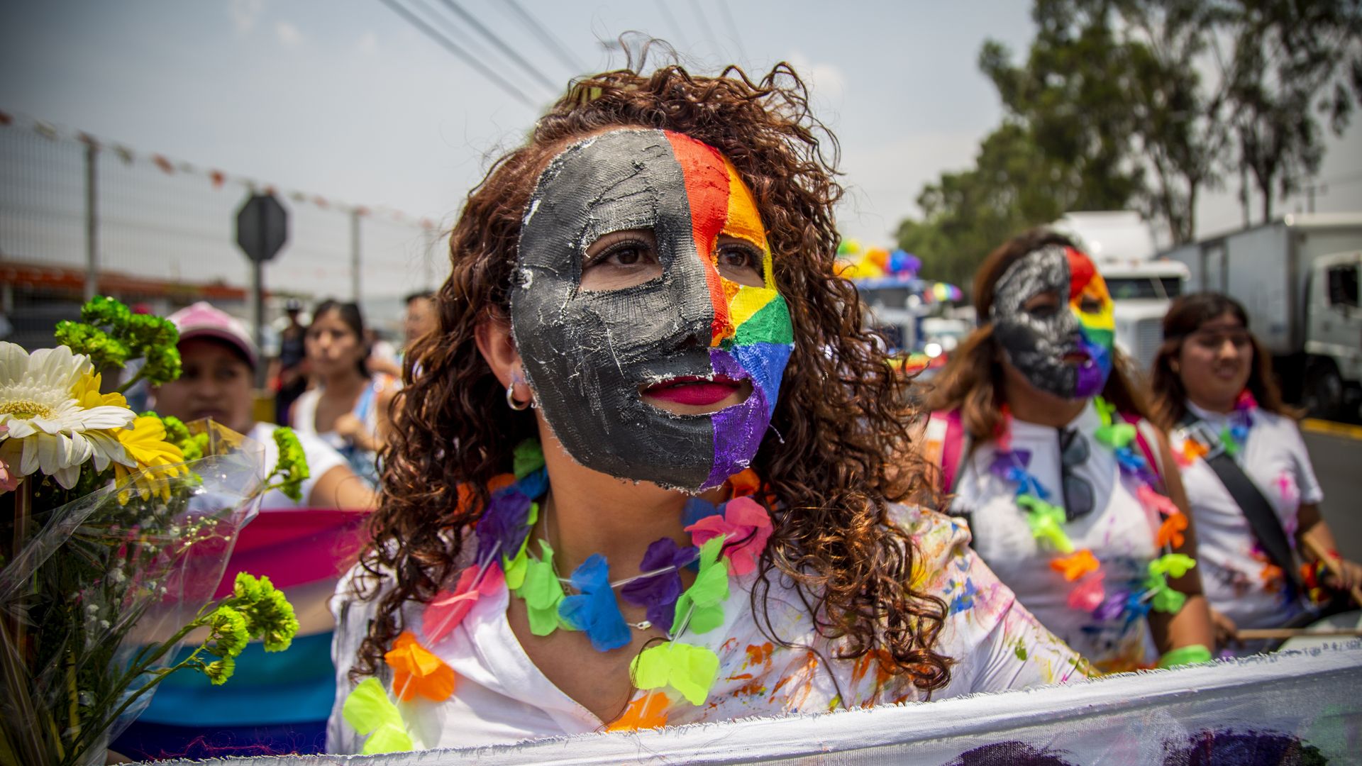 People wearing colorful masks and leis while holding signs against homophobia