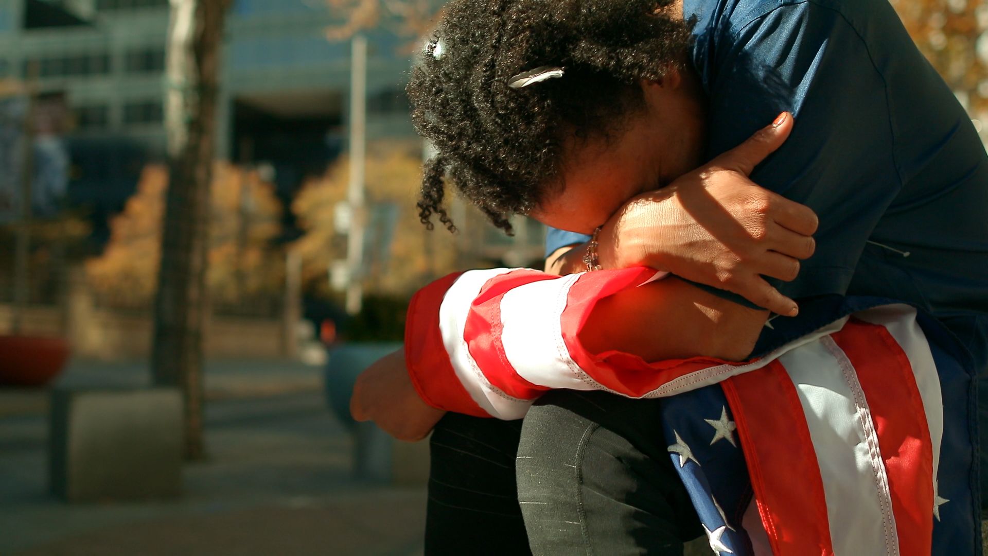 A person bows down and holds their hands over their knees with an American flag.