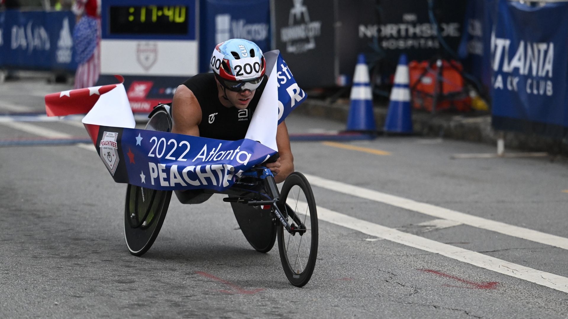 A man using a racing wheelchair speeds into the finish line at the Peachtree Road Race wheelchair division