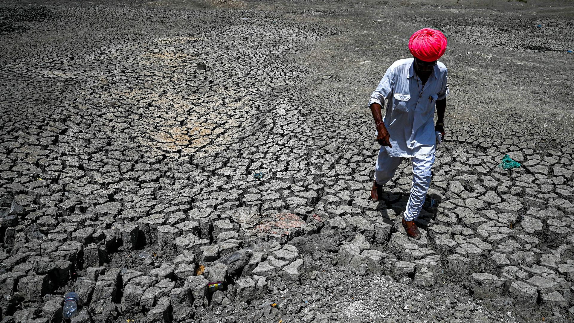A villager walking through the cracked bottom of a dried-out pond on a hot summer day at Bandai village, India.