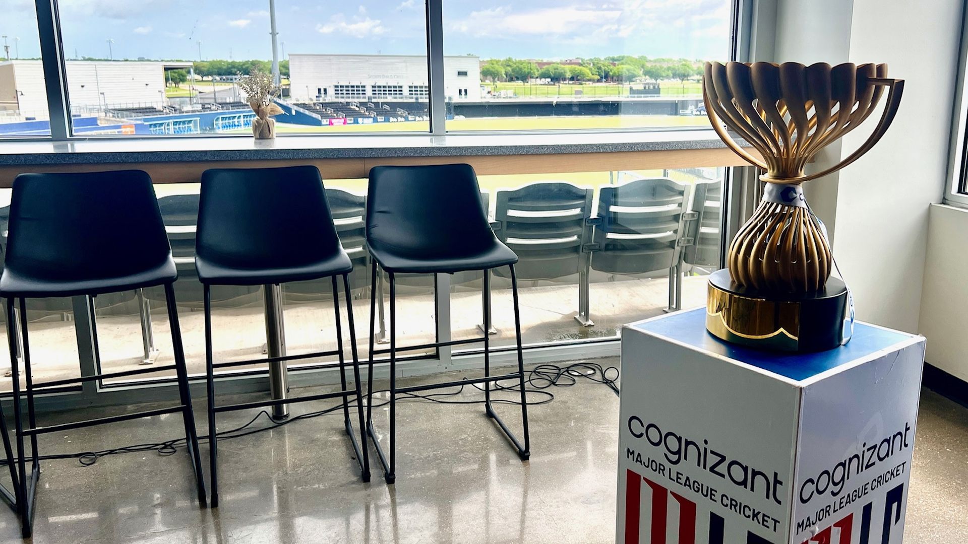 A bronze trophy sits on a white pedestal with a stadium behind it