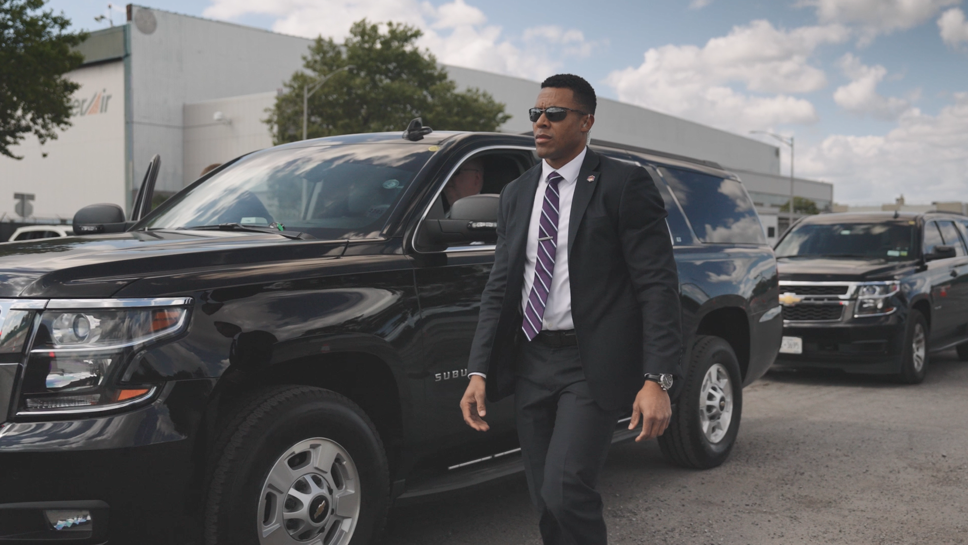 A DSS special agent in a black suit in front of two black SUVs