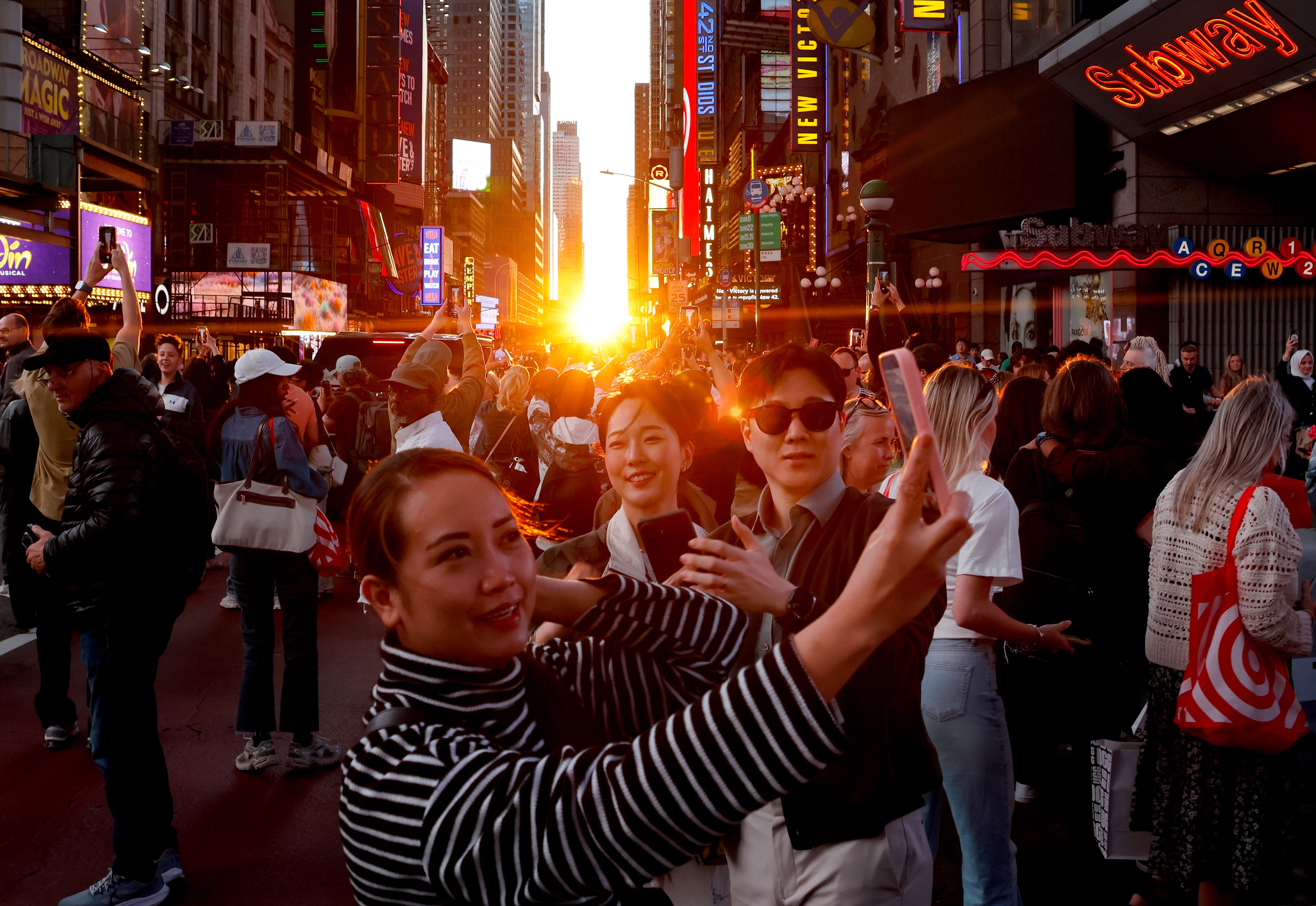 People take pictures during a Manhattanhenge sunset along 42nd Street in Times Square on May 28, 2026, in New York City. (Photo by Gary Hershorn/Getty Images)
