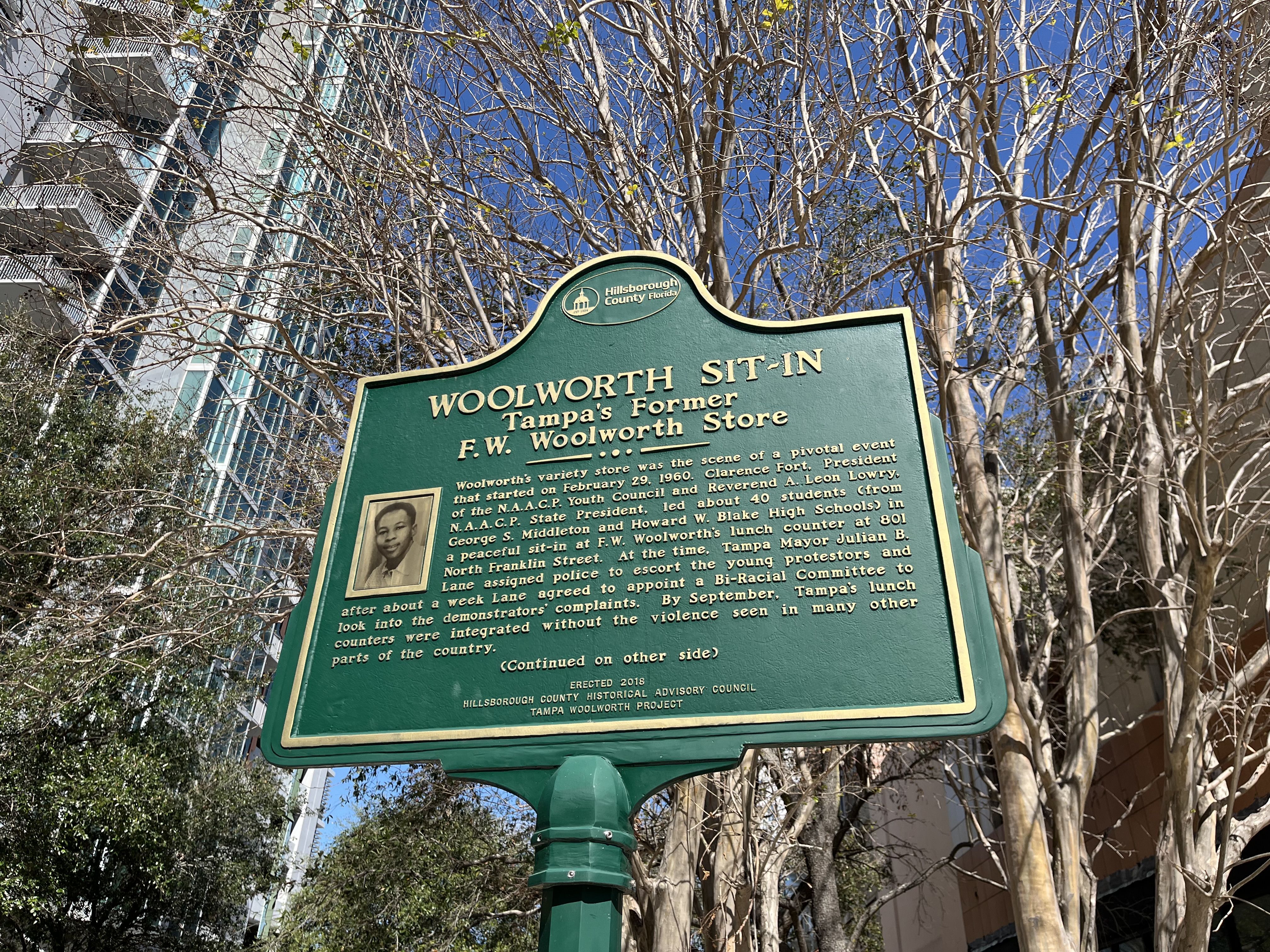 A green historic marker with gold text that reads "WOOLWORTH SIT-IN Tampa's former F.W. Woolworth Store."