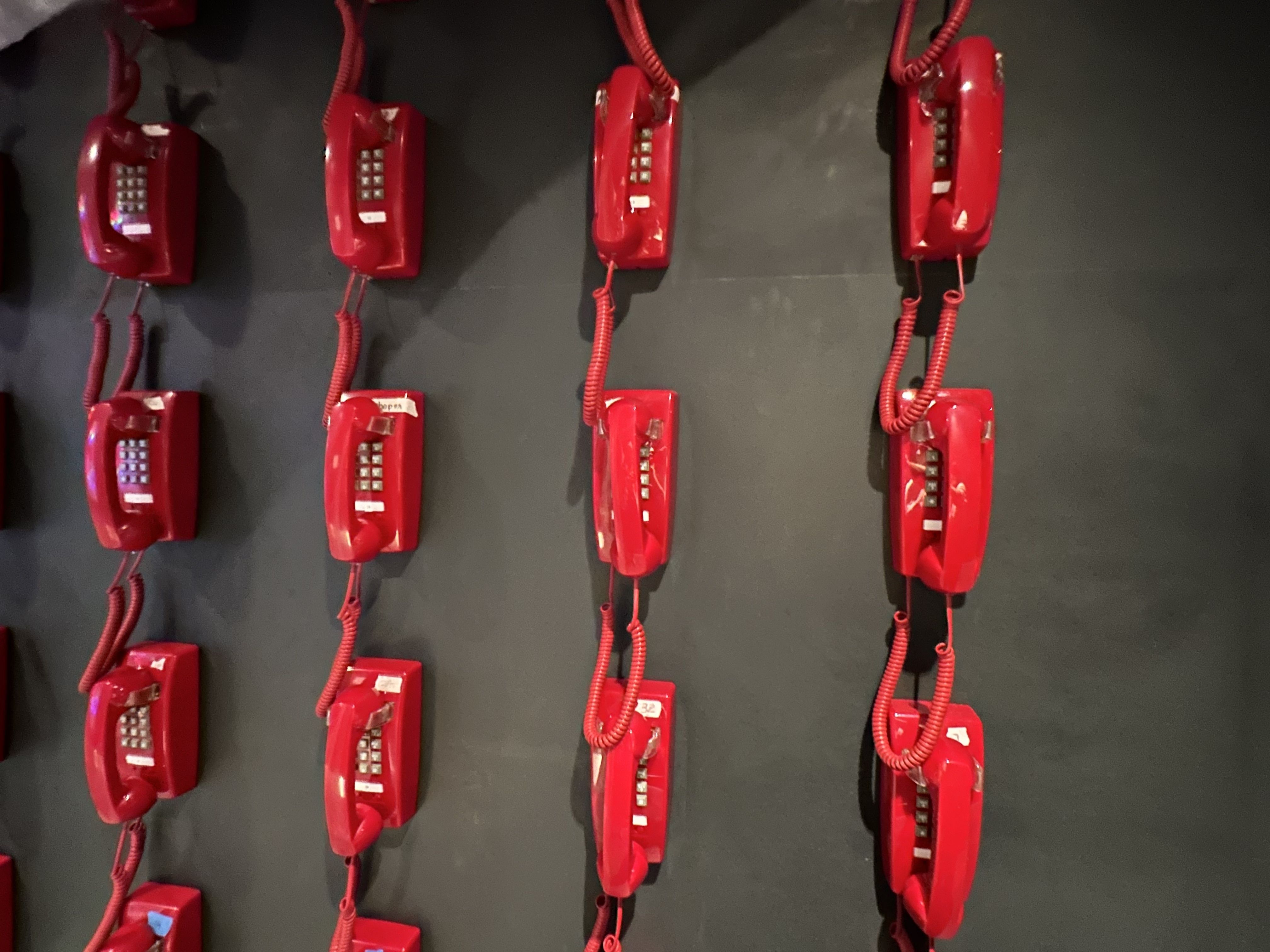 A wall with dozens of red telephones that hang on the wall, each playing a voice of a different changemaker as part of an exhibit at the WNDR Museum Boston.