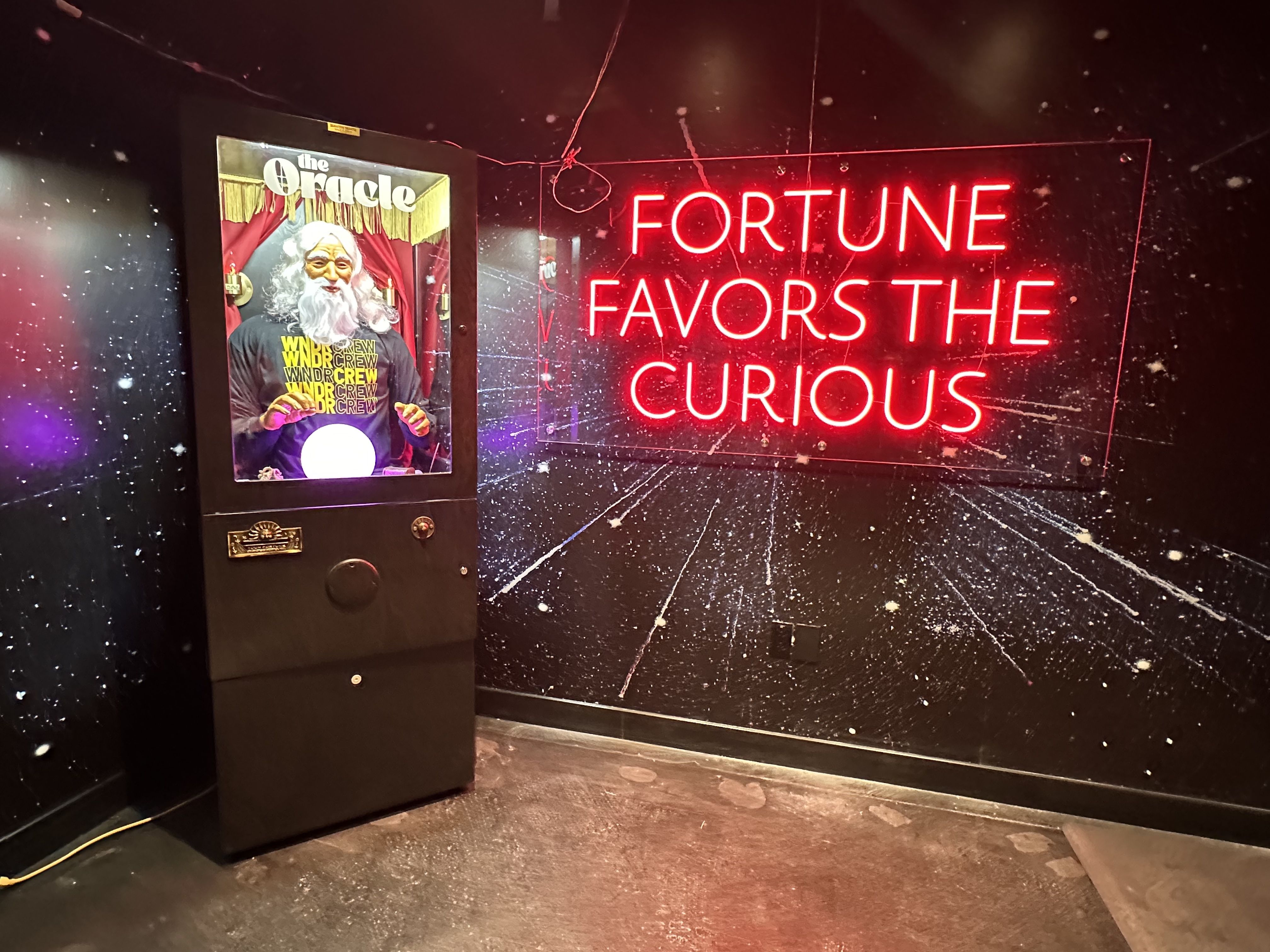 The WNDR Museum includes an installation of a white-haired man looking into a crystal ball, next to a sign that says "fortune favors the curious."