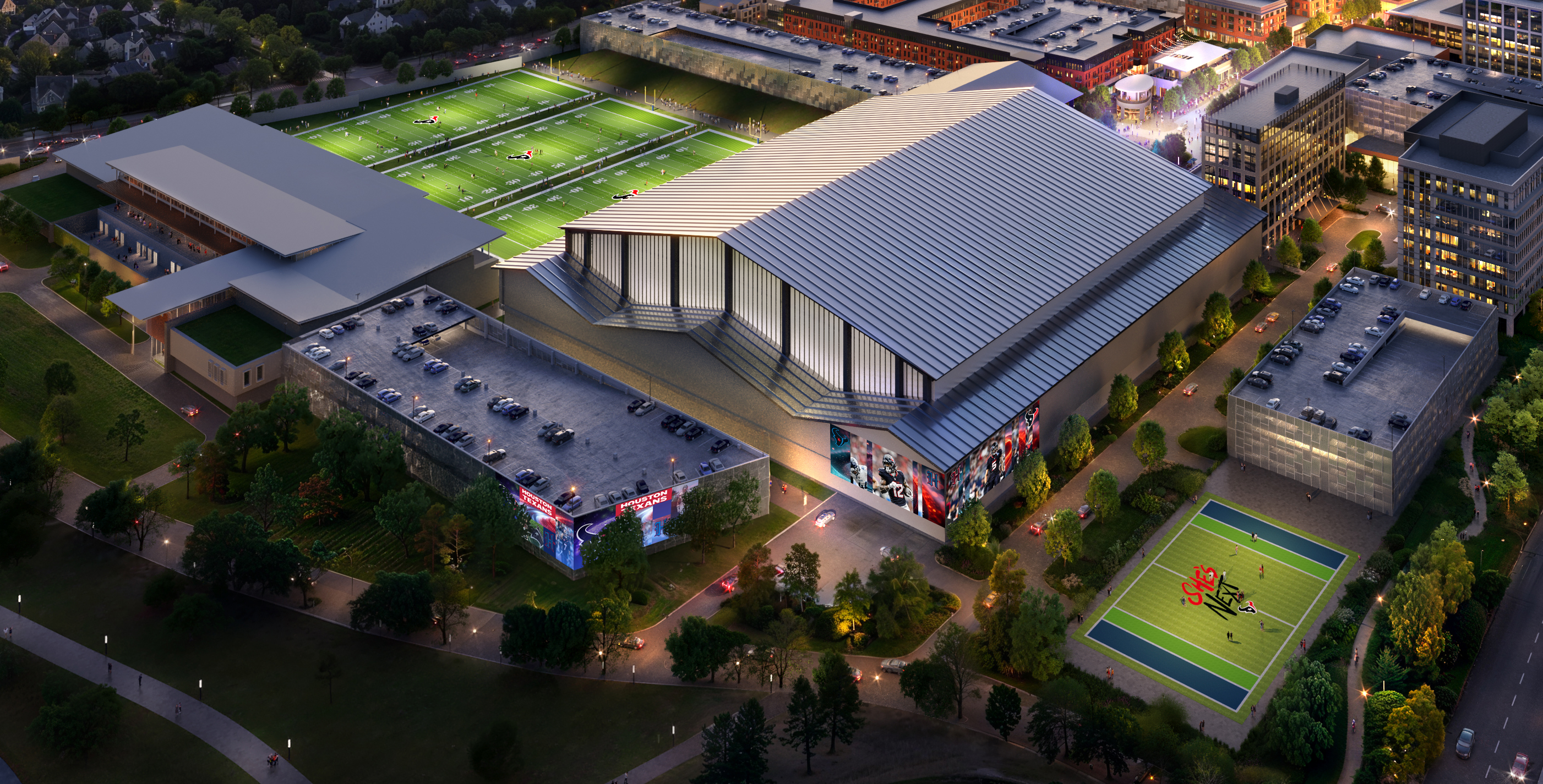 Aerial night view of a large sports complex with illuminated football fields, parking lots on rooftops, and modern buildings surrounded by trees and city lights.