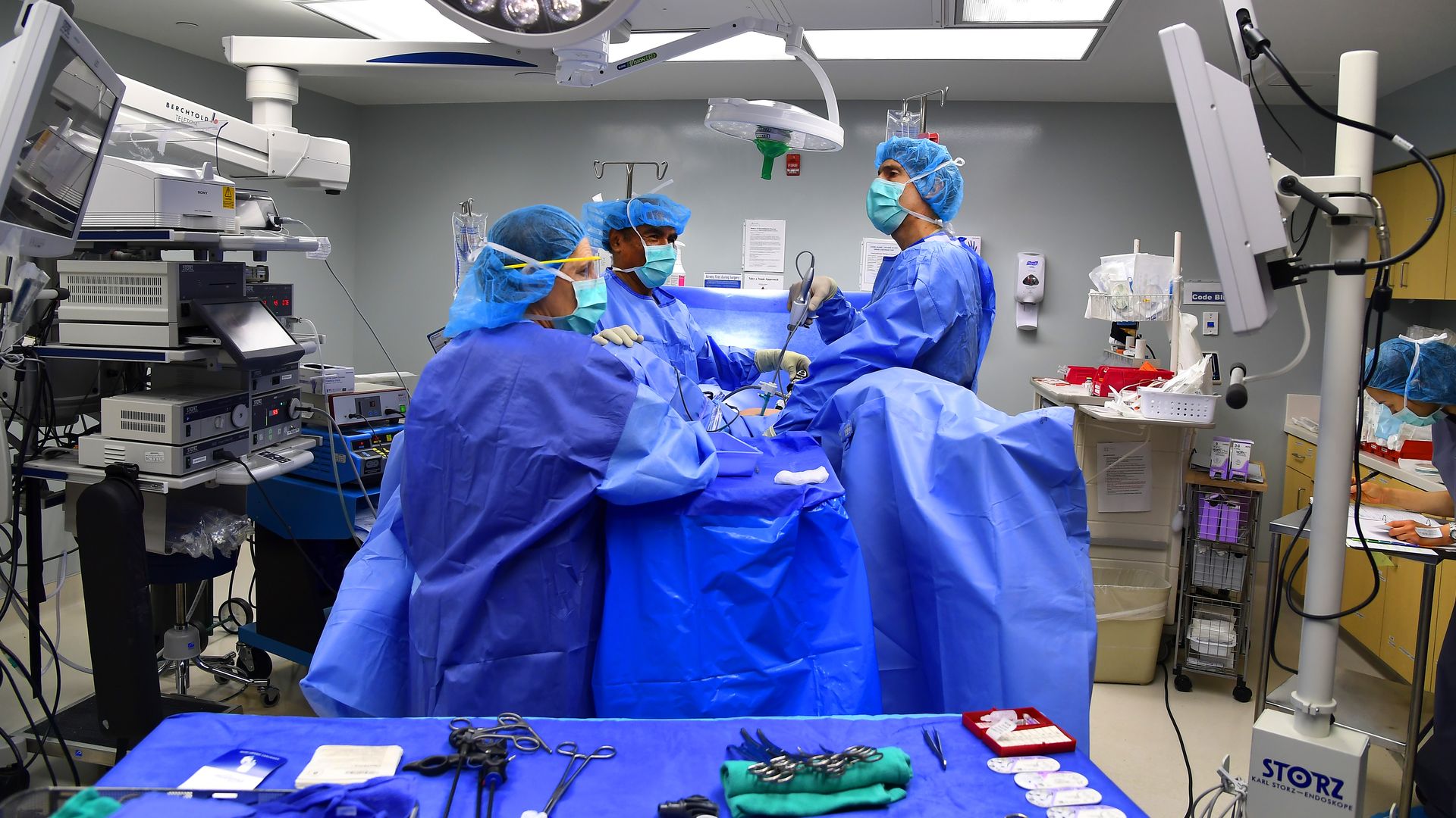 Doctors dressed in blue operate on a patient in a surgical suite.