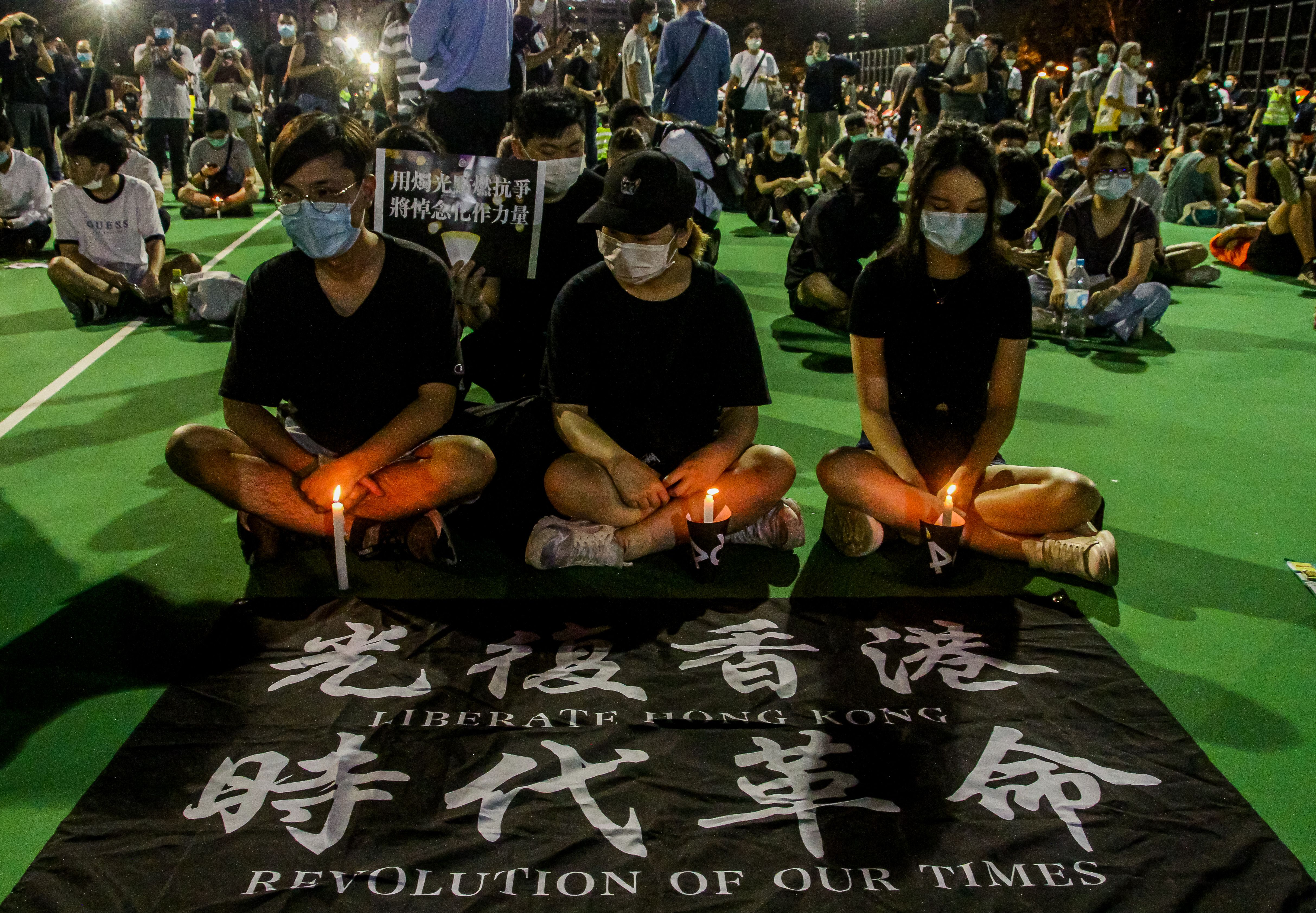 Three people wearing face masks sit cross-legged in front of a banner