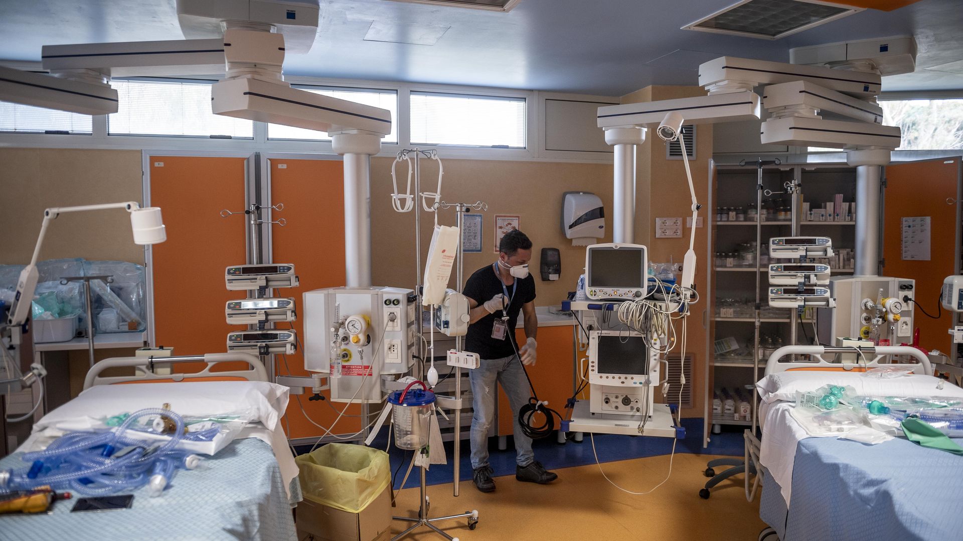 A man prepares an intensive care unit surrounded by beds and other hospital equipment.