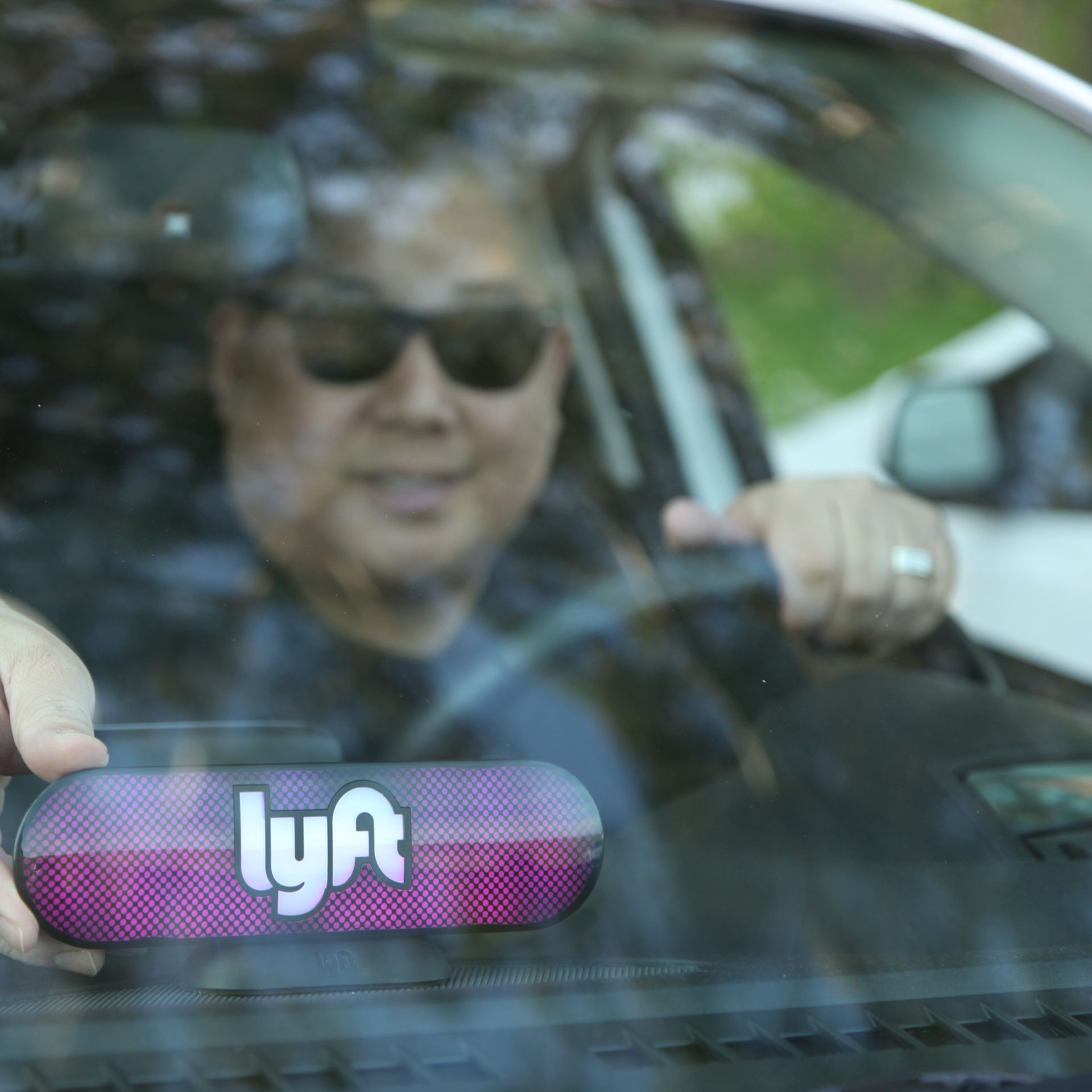 Driver behind the wheel with an illuminated Lyft sign on dashboard