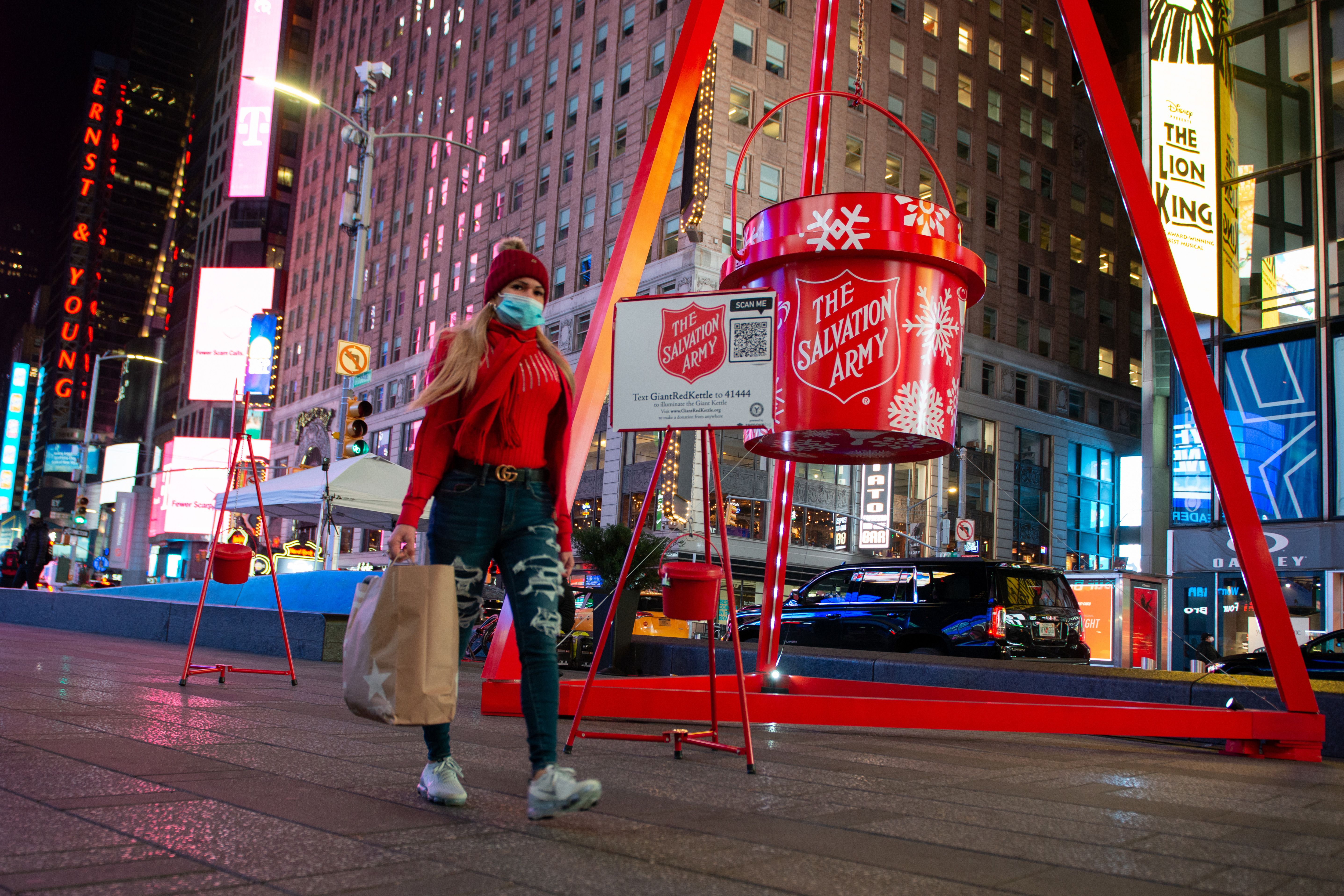 A woman wearing a mask walks past The Salvation Army's Giant Red Kettle in Times Square on December 02, 2020 in New York City.