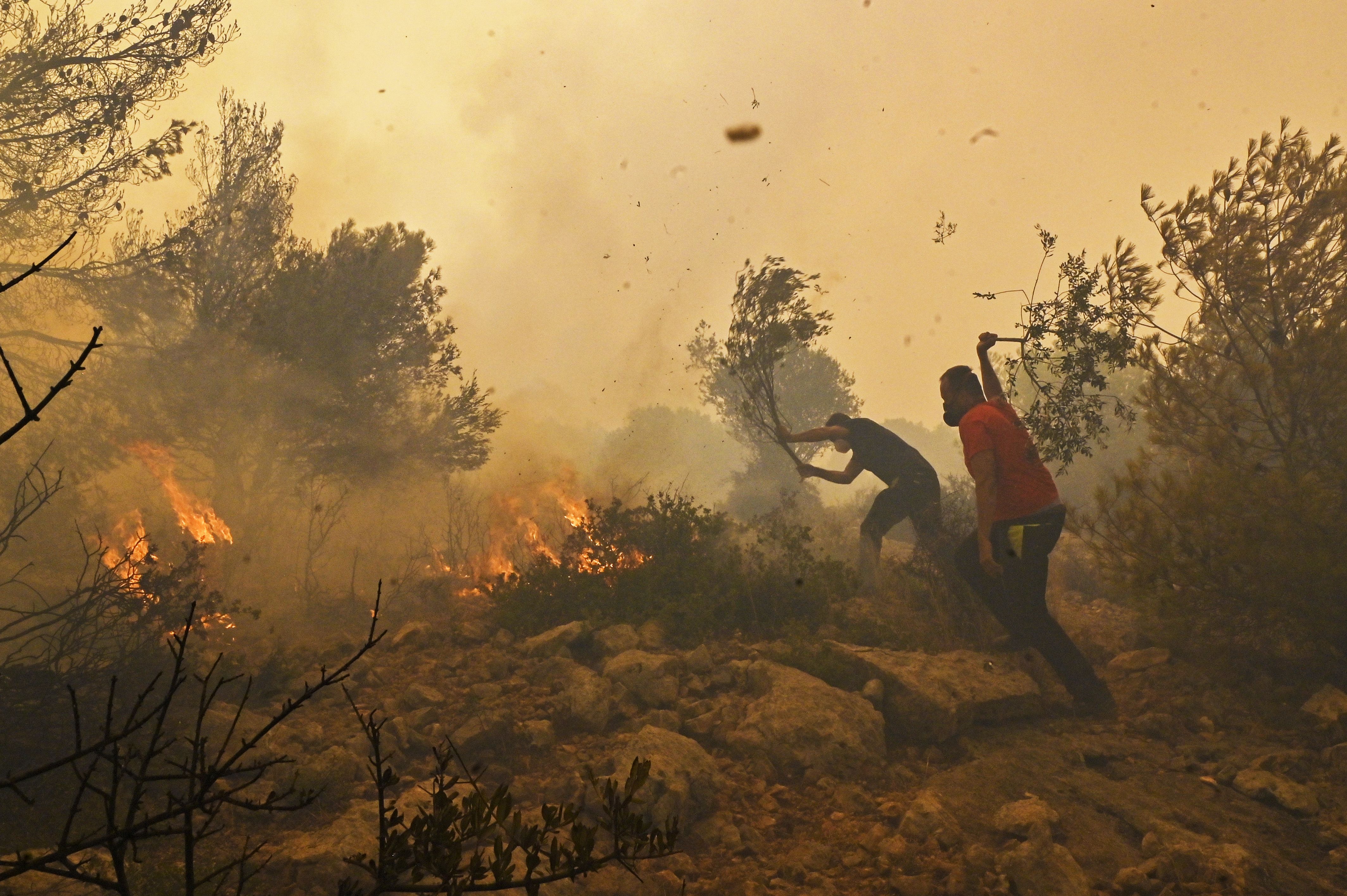 Locals help firefighters as they try to extinguish a wildfire burning near the village Vlyhada near Athens on July 19, 2023 in Athens, Greece. Several forest fires raged on the outskirts of the Greek capital amid a relentless heatwave, with the most violent fire in the forest of Dervenohoria 50 km north of Athens where 140 firefighters, six water bombers and a helicopter battled the flames during high winds. France and Italy have sent planes to support the operation. The Acropolis of Athens and other archaeological sites in Greece announced reduced opening hours due to the heatwave conditions. 