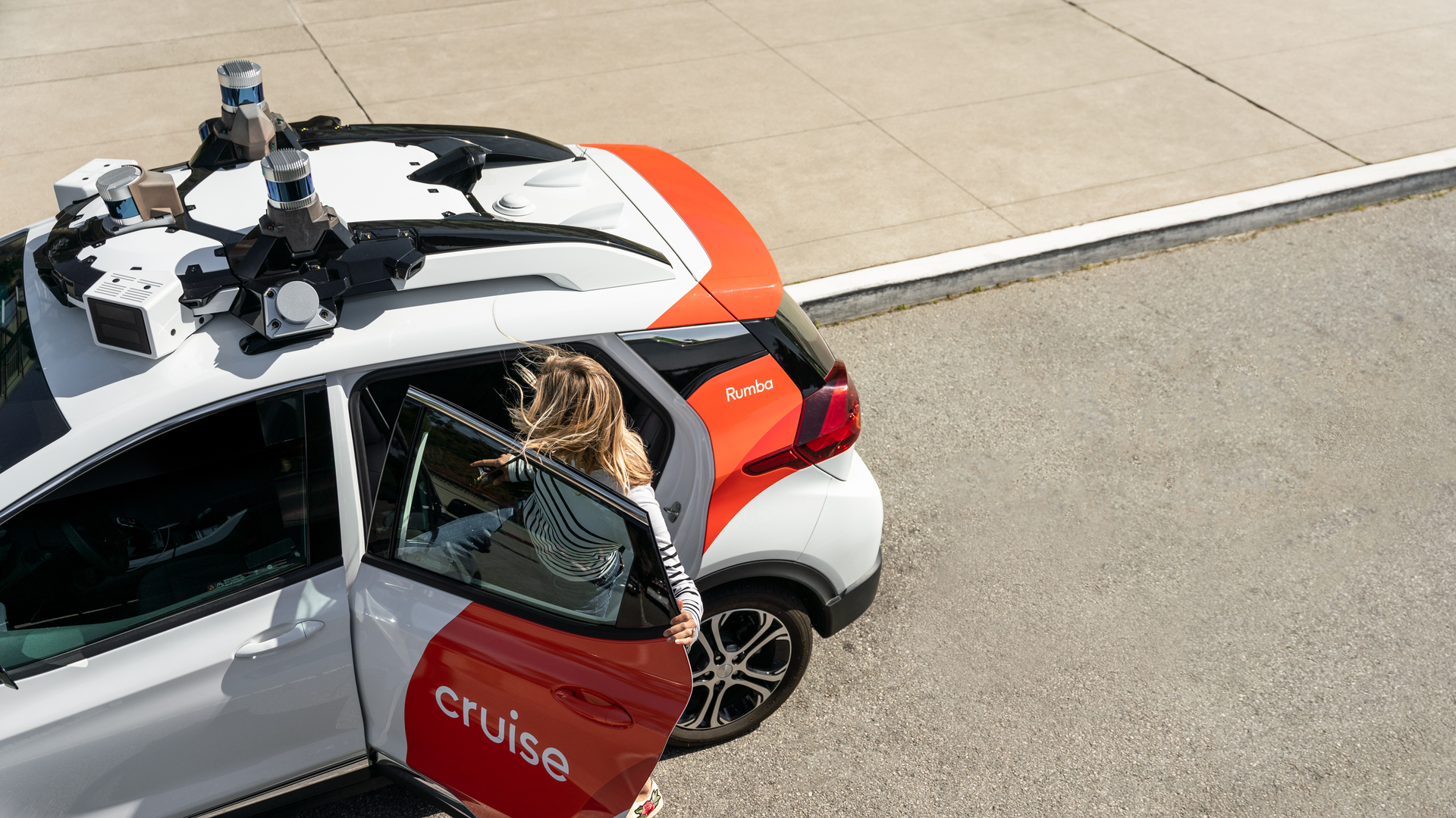 A woman exits a self-driving taxi that says Cruise on the door and has equipment on the top