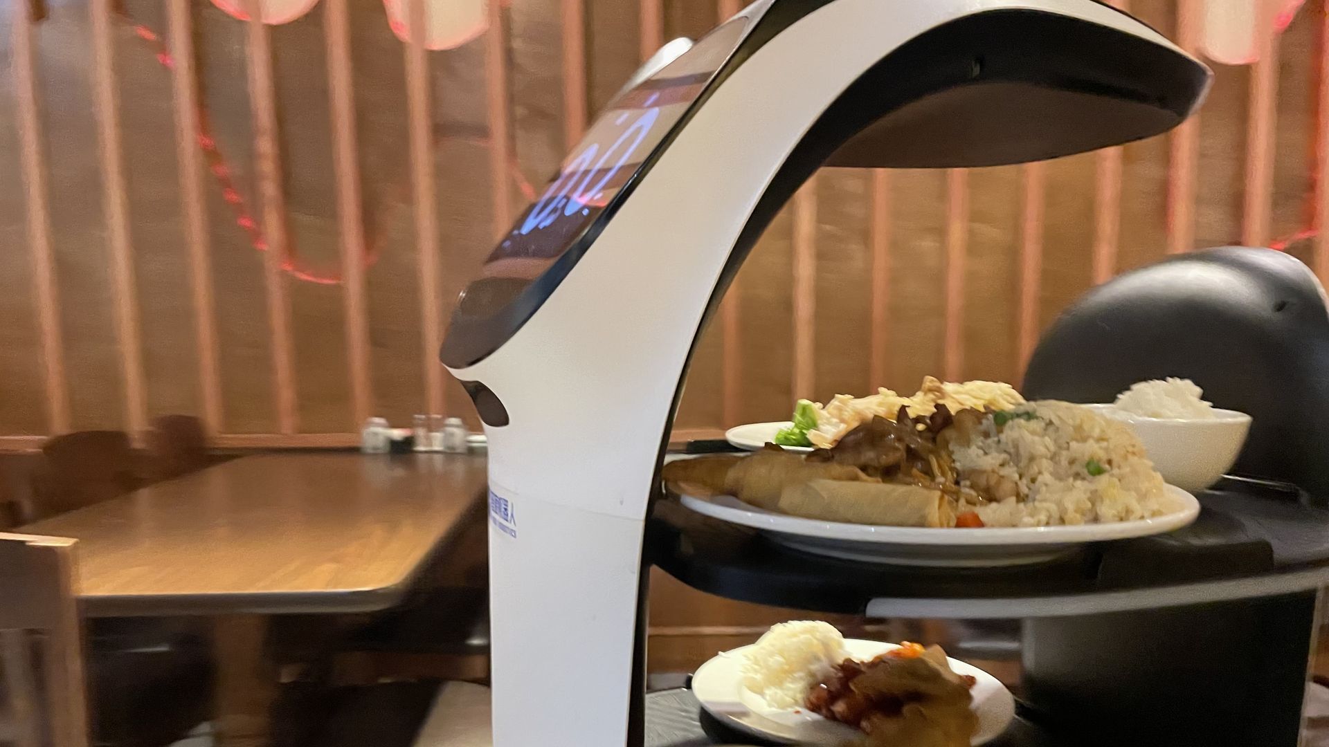 A sleek, white robot shaped like a scooter carries food on trays.