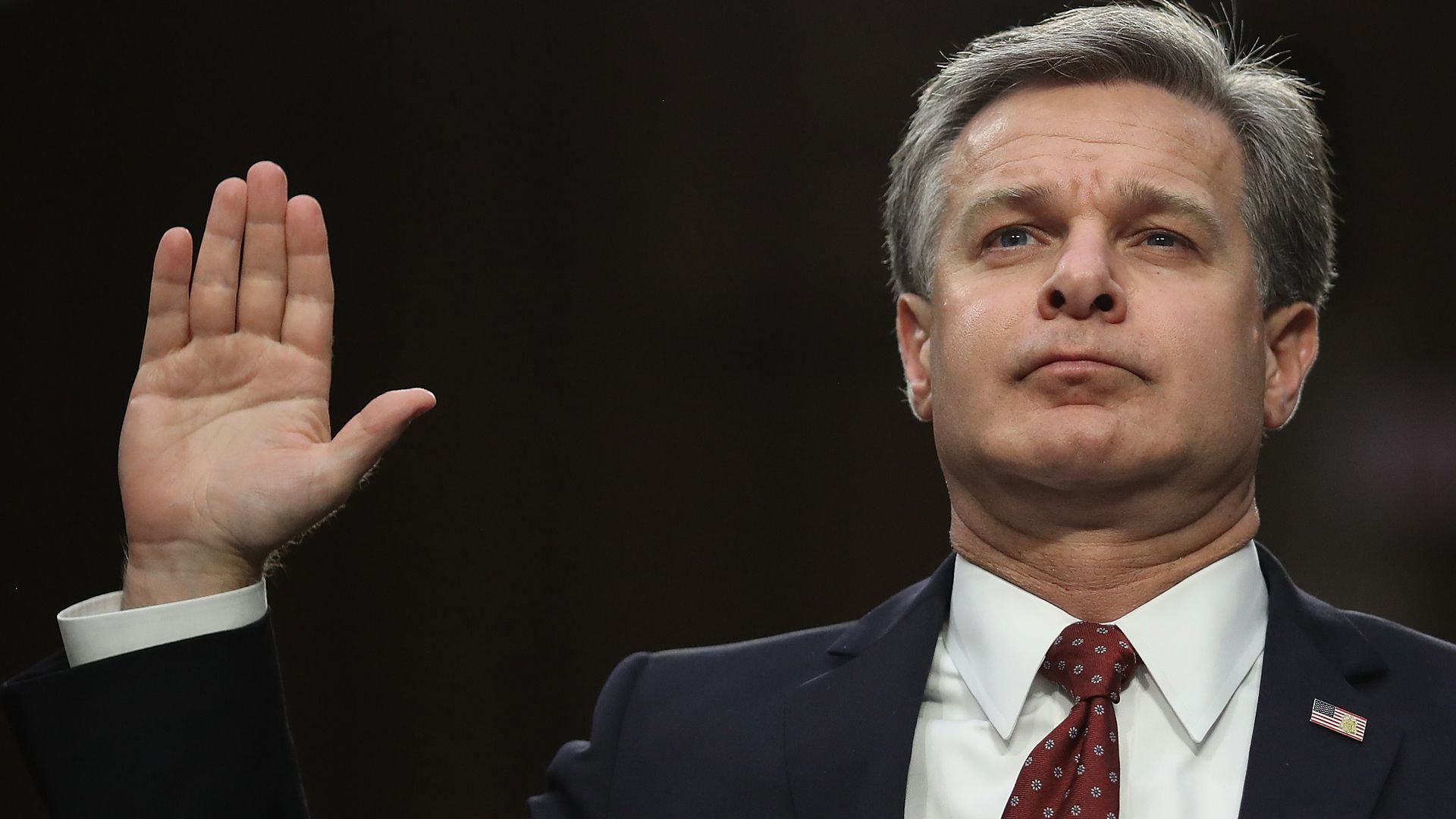 Photo of FBI Director Christopher Wray holding his right hand up in the air 