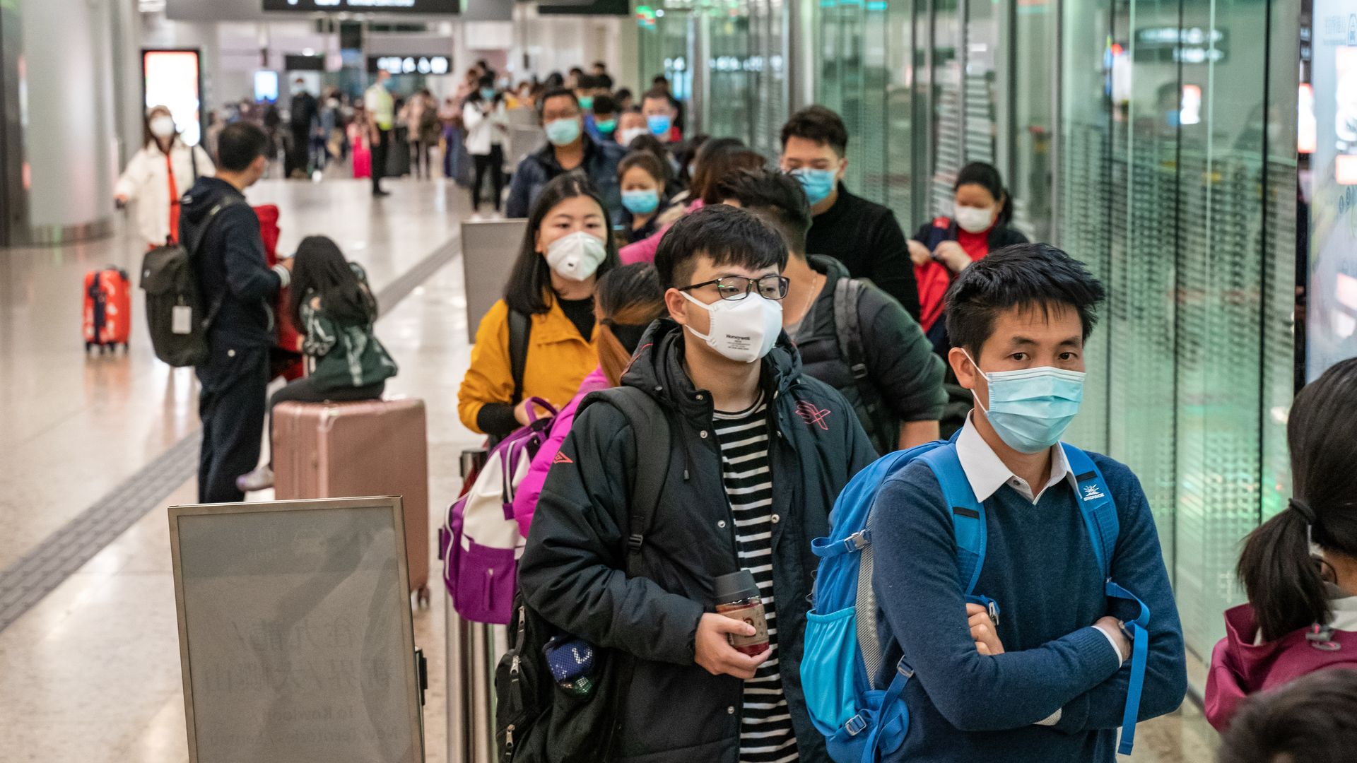 In this image, a line of people wearing face masks to protect against the coronavirus stand in line.