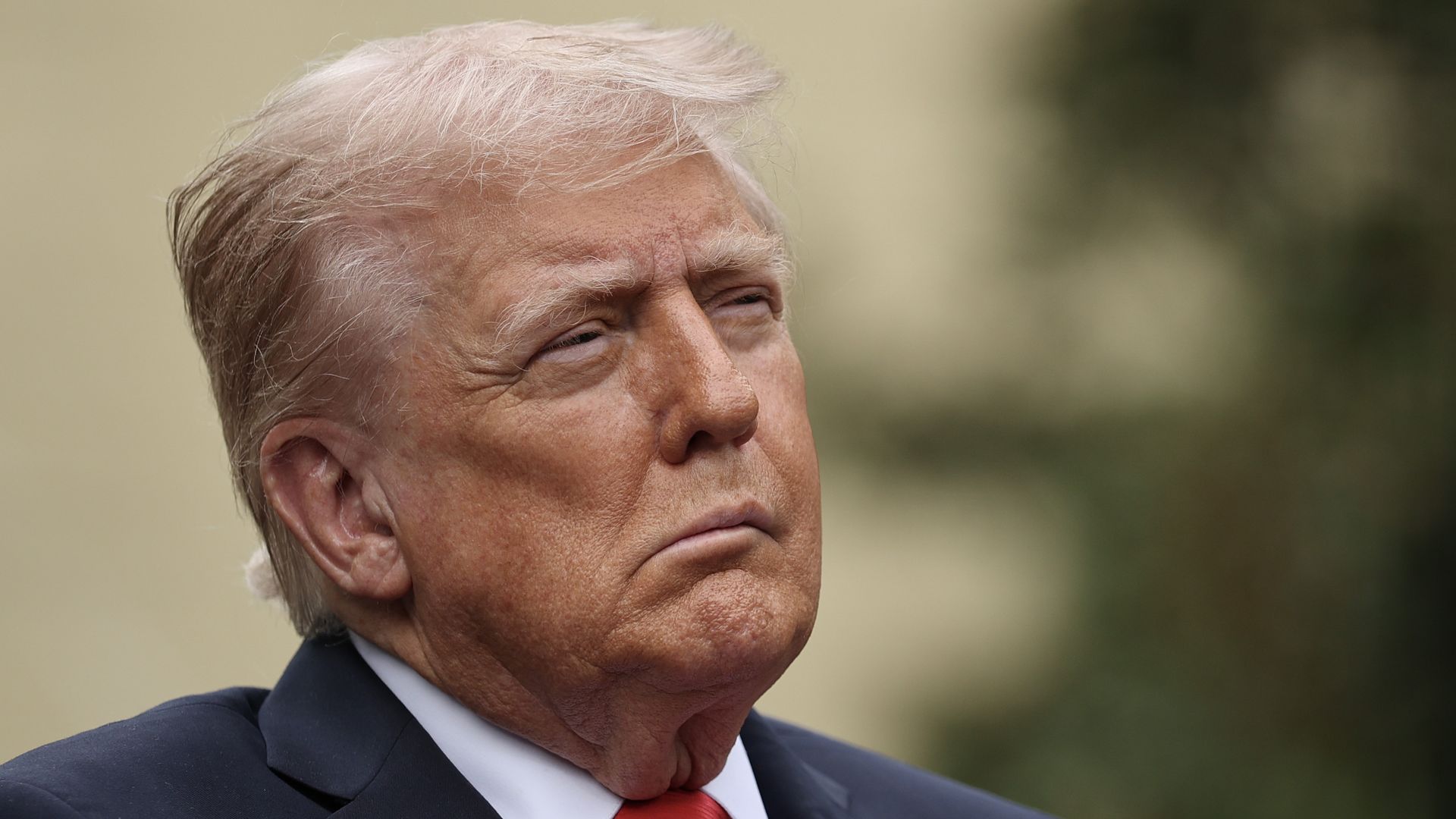 A headshot of a squinting President Trump, wearing a navy jacket, white shirt and red tie.