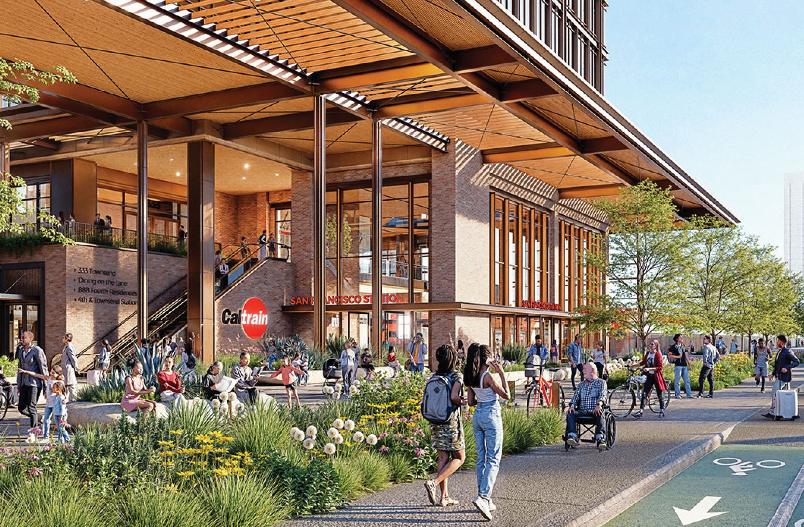 Modern transit plaza beside a brick building with tall windows and a wooden canopy. People walk, bike, and a person in a wheelchair uses a bike lane beside flowering plants.