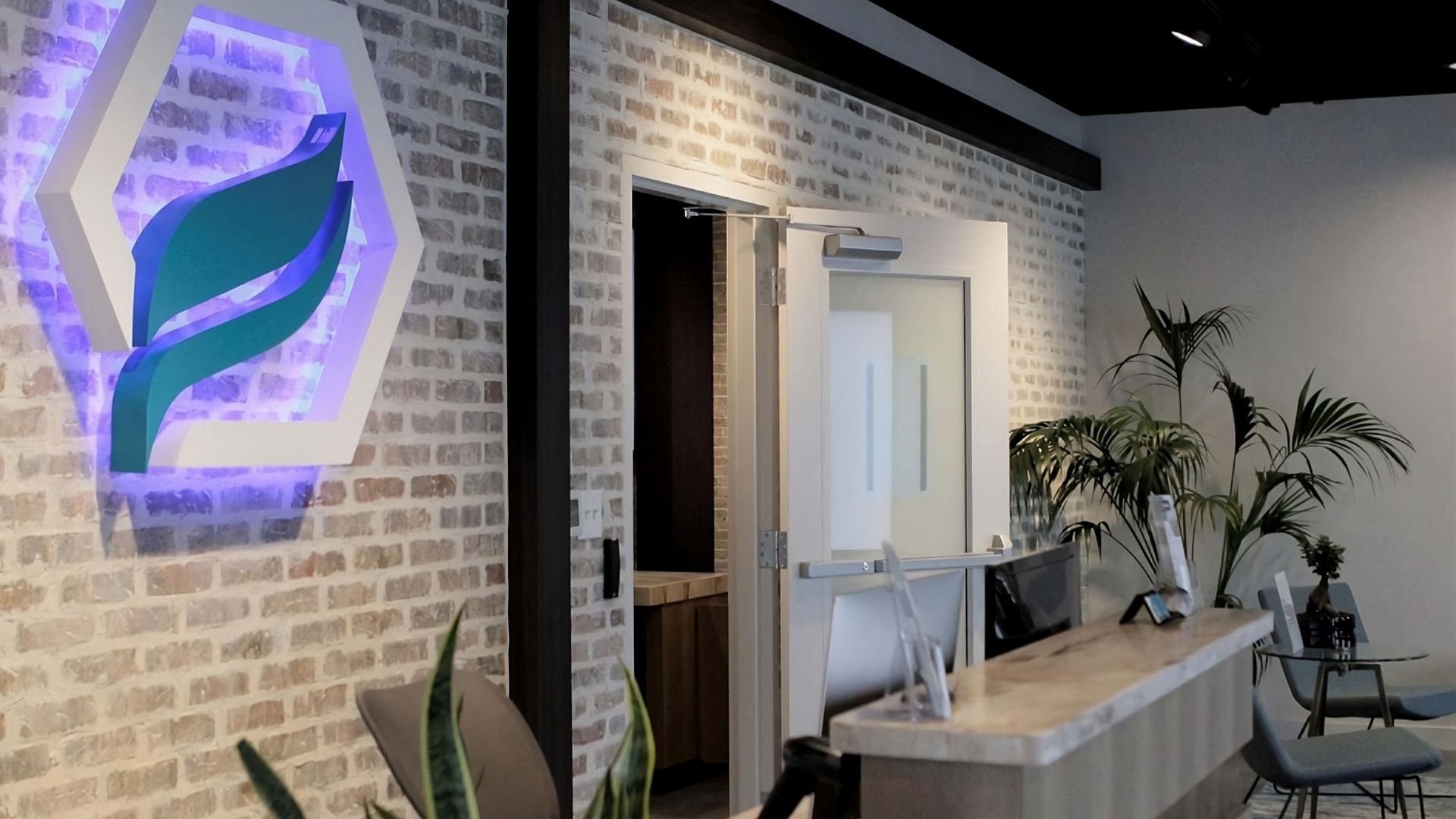 The front desk check-in area of a dispensary, with a brick wall behind it with the lit-up Terrasana logo on it