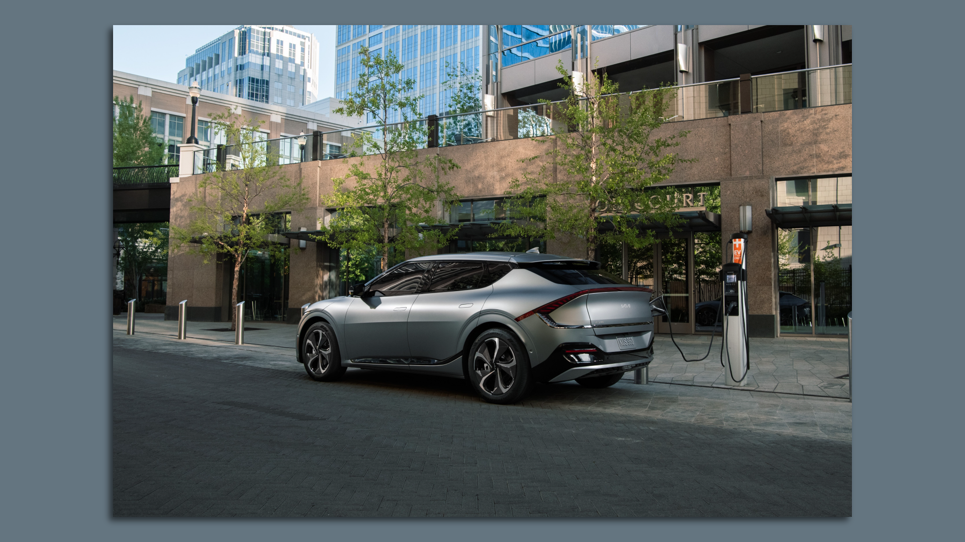 Photo of a Kia EV6 plugged into a charging station on an urban street.
