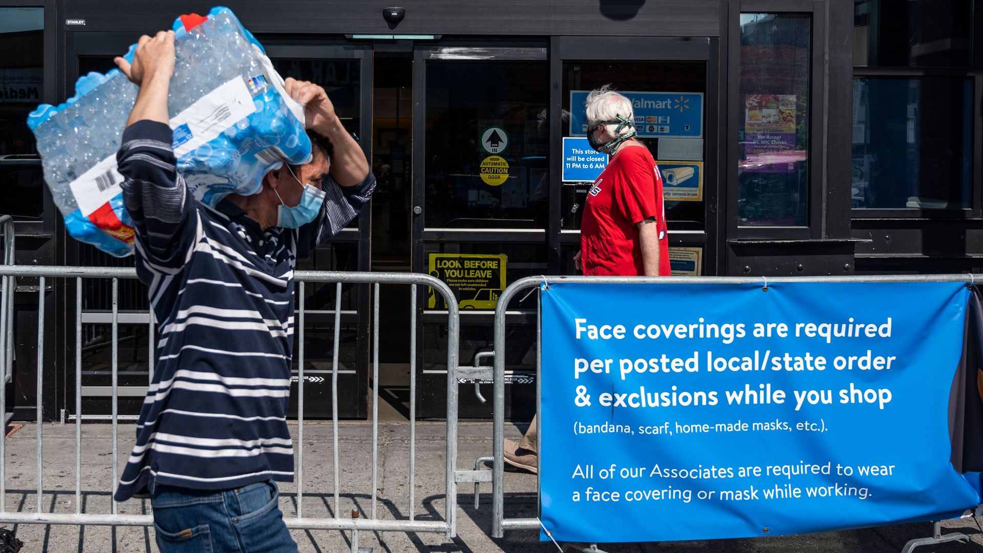 Shoppers wearing facemasks walk near a sign informing customers that face coverings are required in front of a Walmart store in Washington, DC 