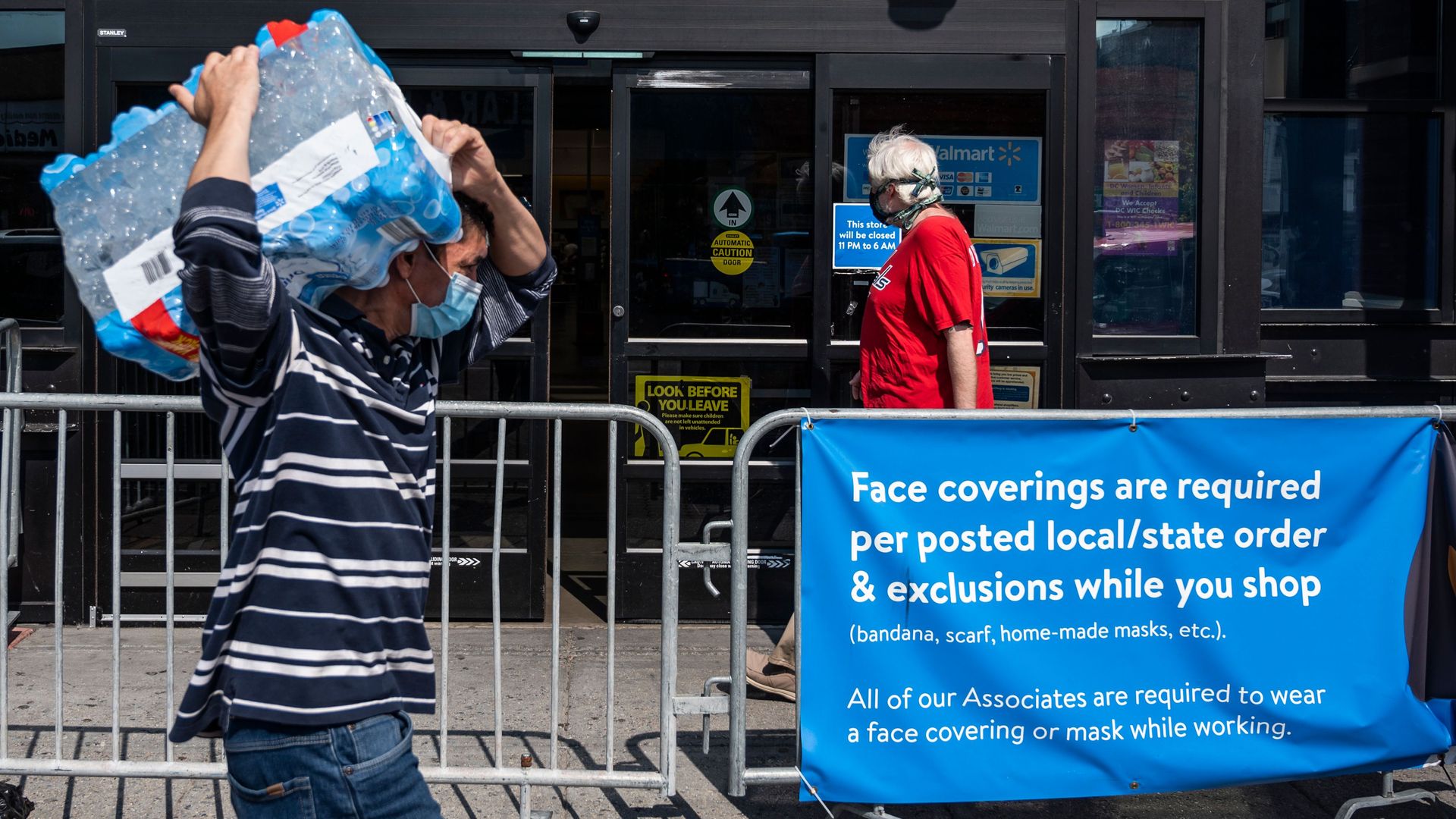 Shoppers wearing facemasks walk near a sign informing customers that face coverings are required in front of a Walmart store in Washington, DC