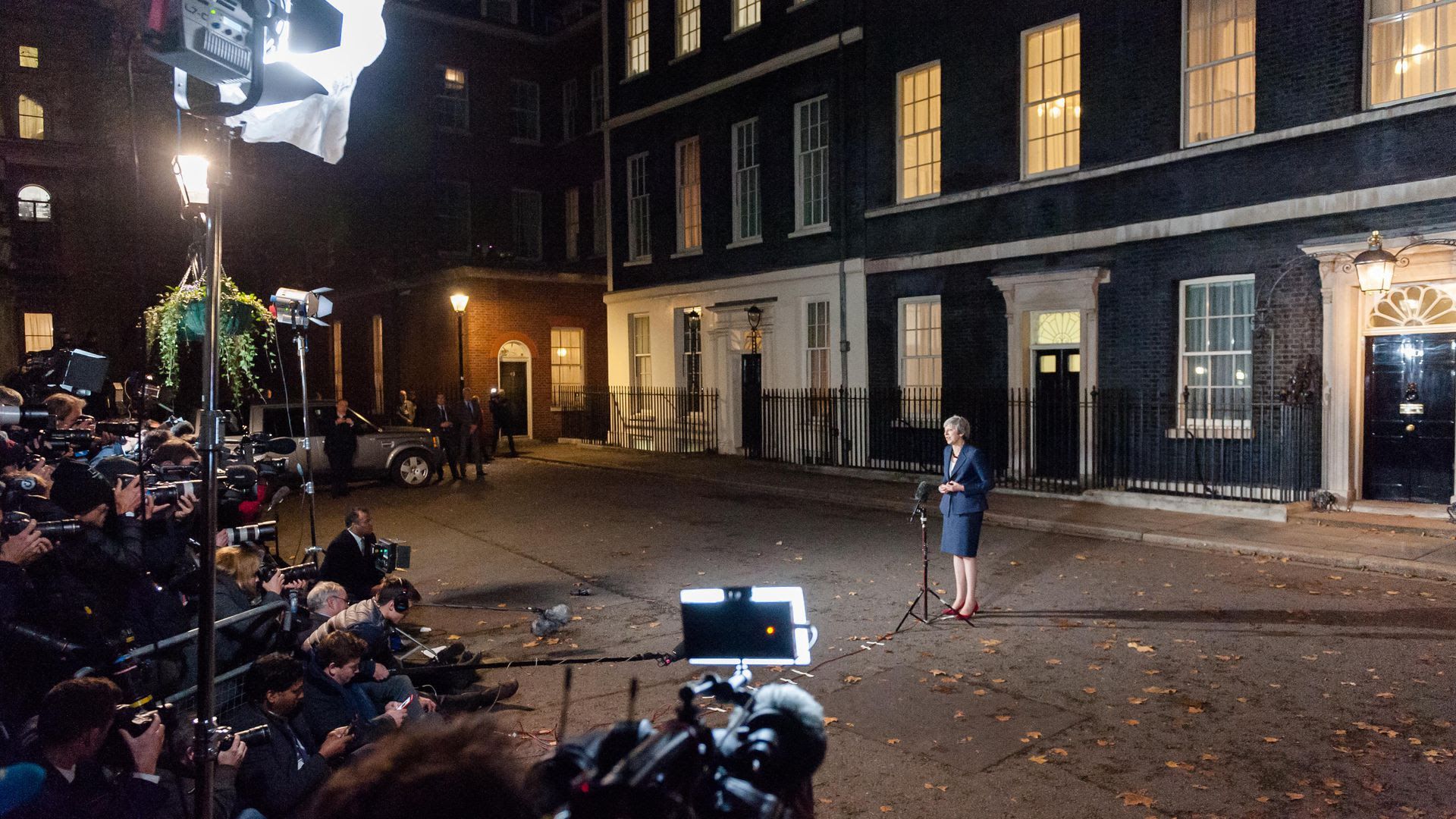 Theresa May stands before a swarm of media at nighttime. 