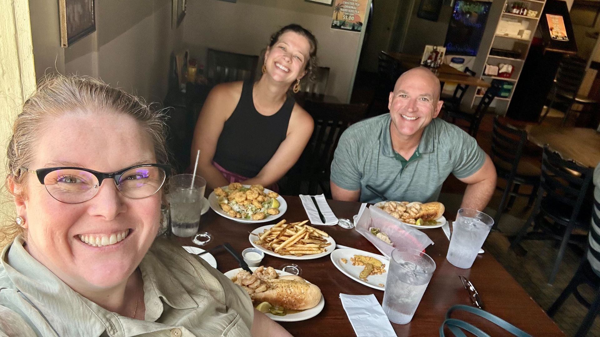 A selfie of three people at a table filled with plate lunches.