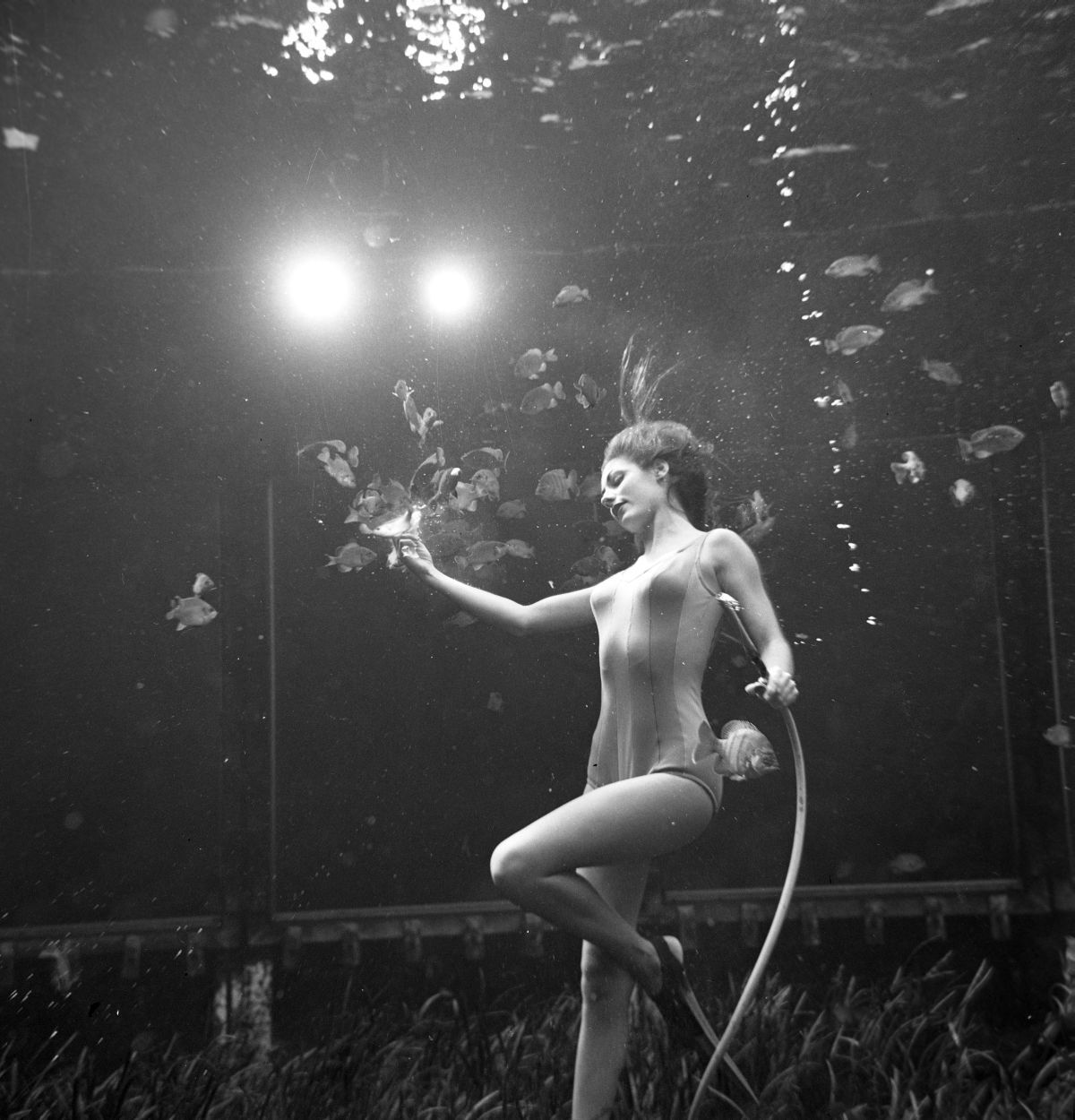 A black-and-white image of a woman in bathing suits practicing a dance routine underwater.