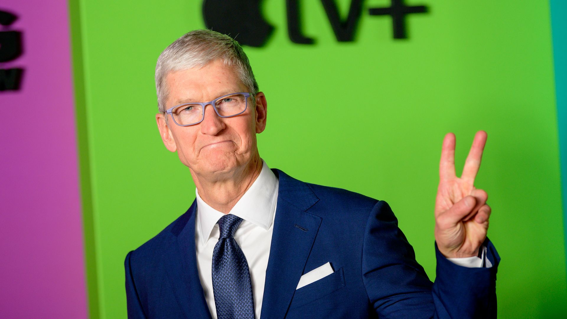 Tim Cook raising a few fingers, with an Apple logo in the background.