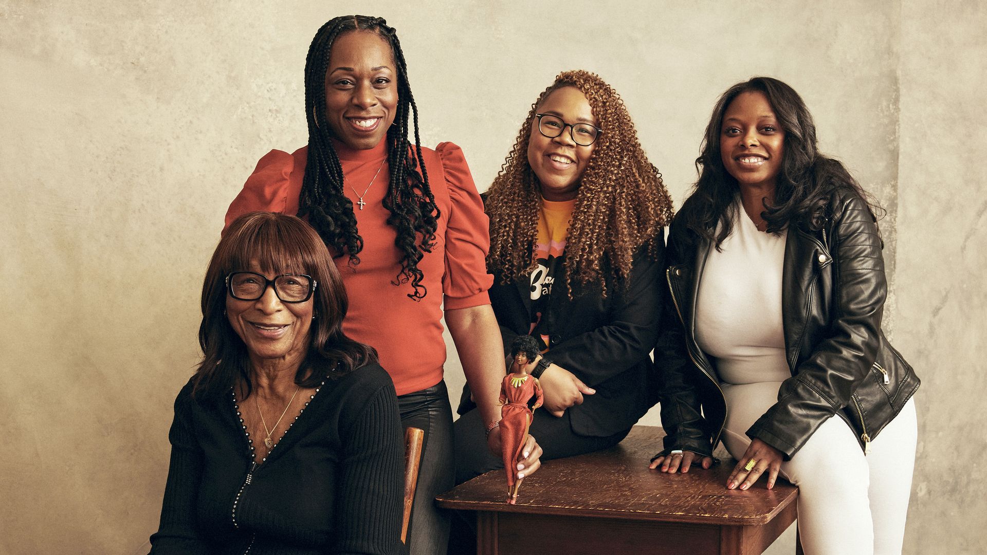 A group of women stand around a table with a Black Barbie doll.