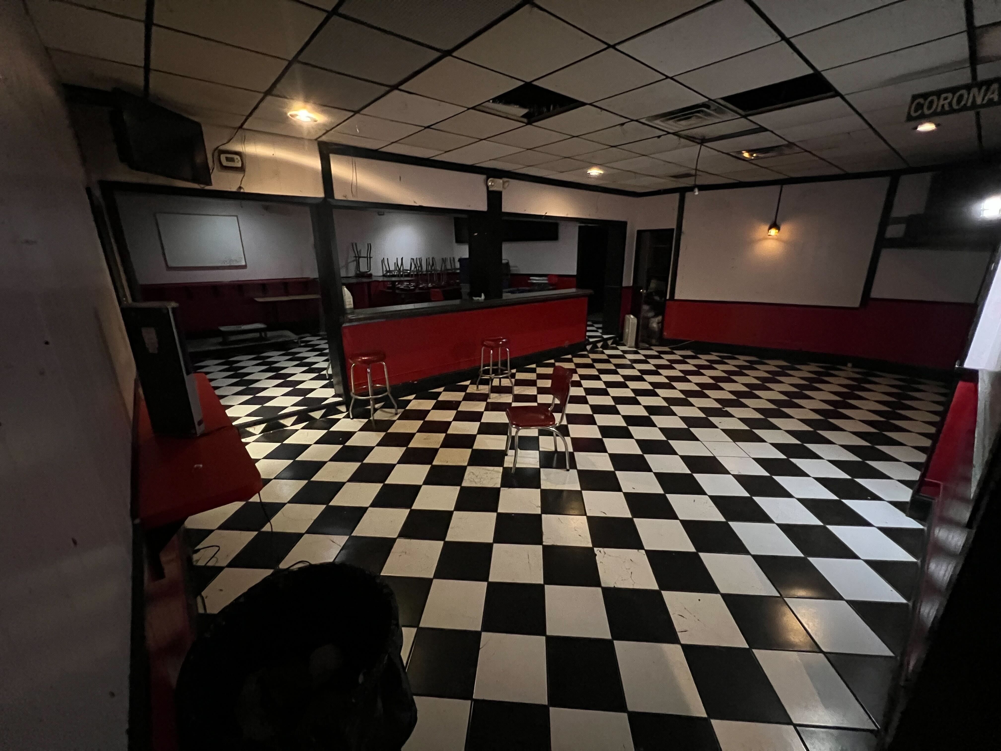 a dark empty bar with  no tables and a a black and white checkered floor and red bar