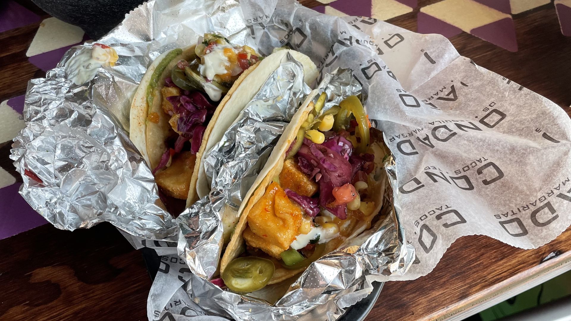 Two tacos wrapped in foil sitting in a basket